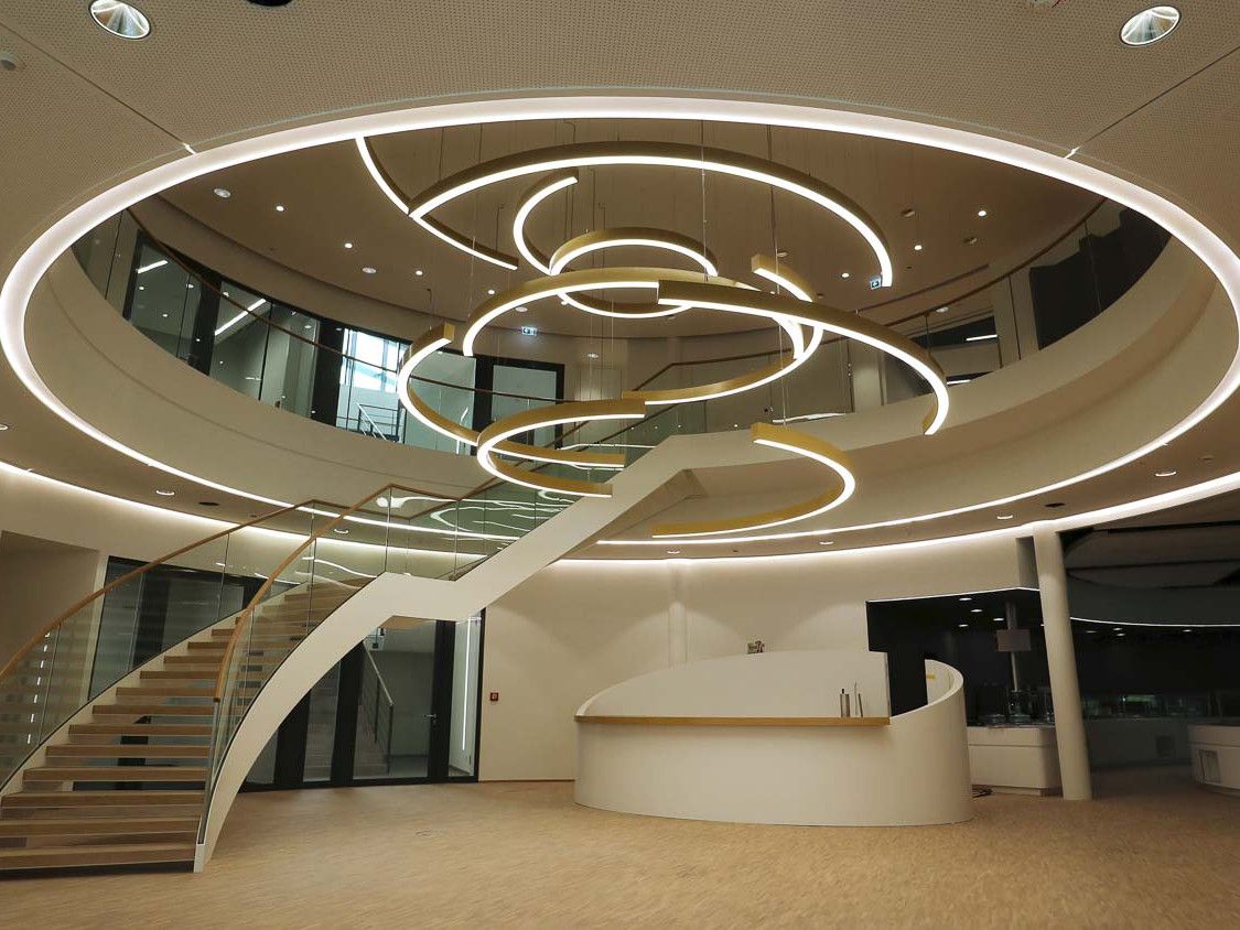 Still aus dem Otto-Quast-Imagefilm: lichtdurchflutetes Foyer mit geschwungener Treppe und Ringleuchten