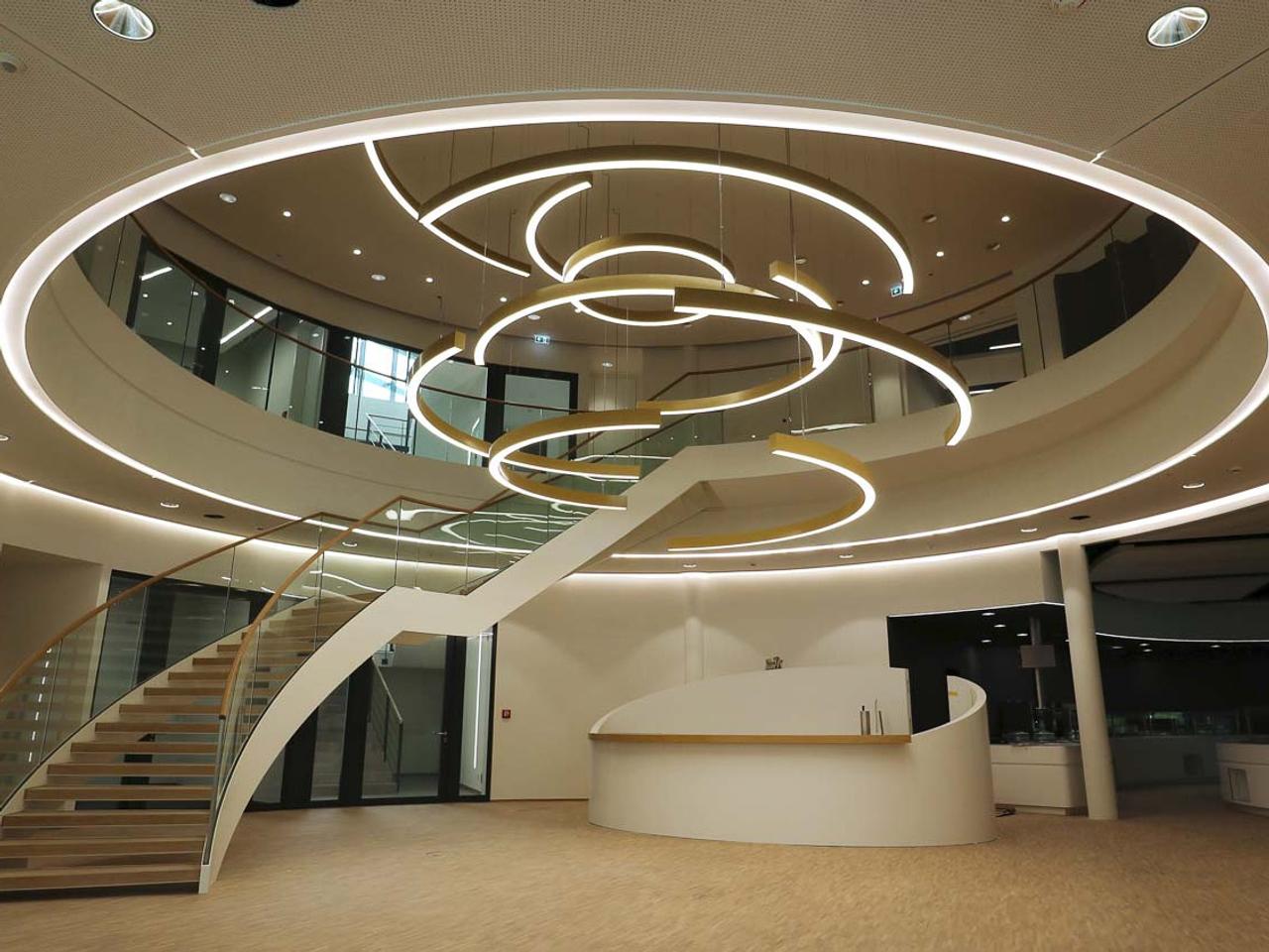 Still aus dem Otto-Quast-Imagefilm: lichtdurchflutetes Foyer mit geschwungener Treppe und Ringleuchten
