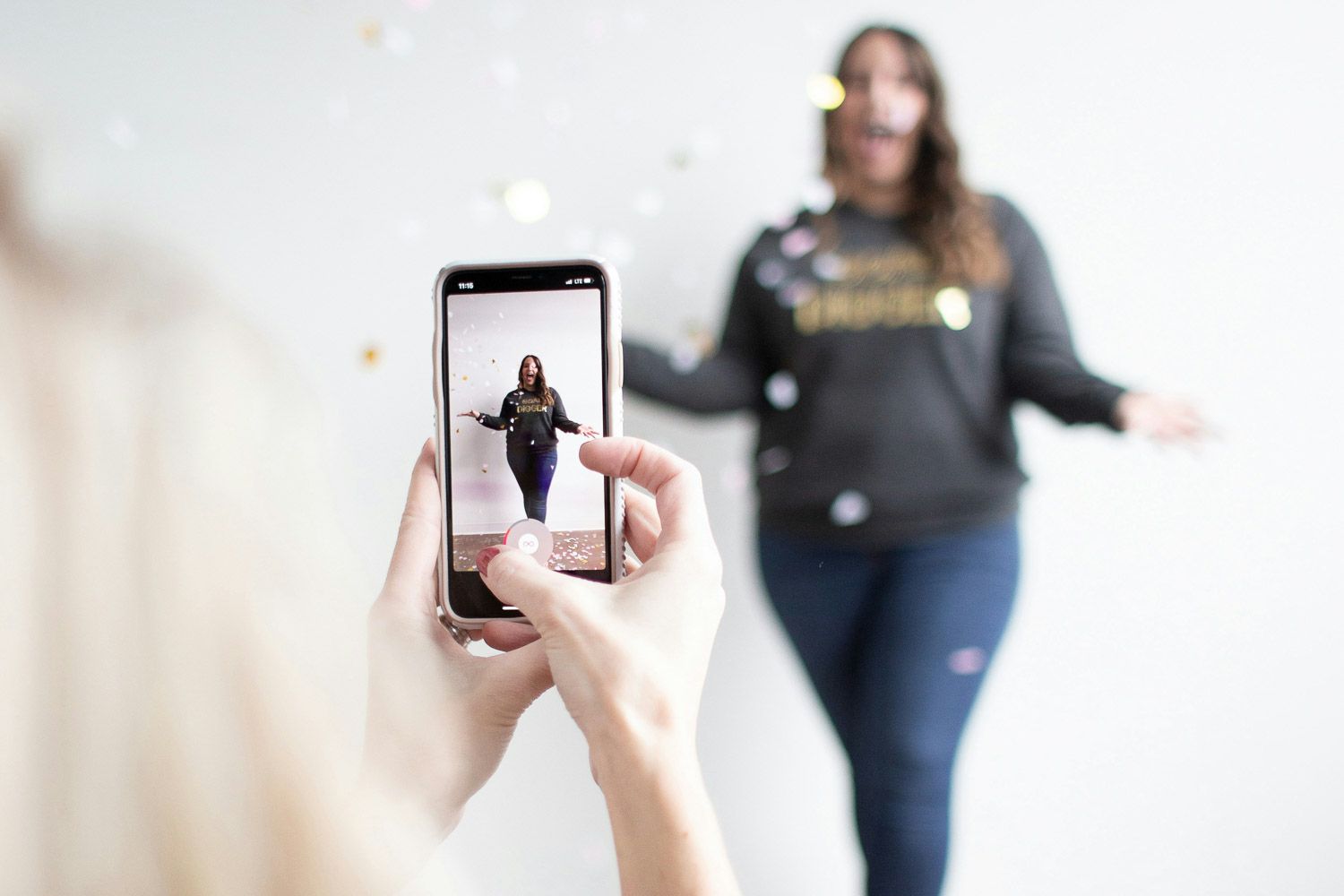 Frau filmt eine Person mit Konfetti per Smartphone – Produktion eines Social-Media-Videos im Studio