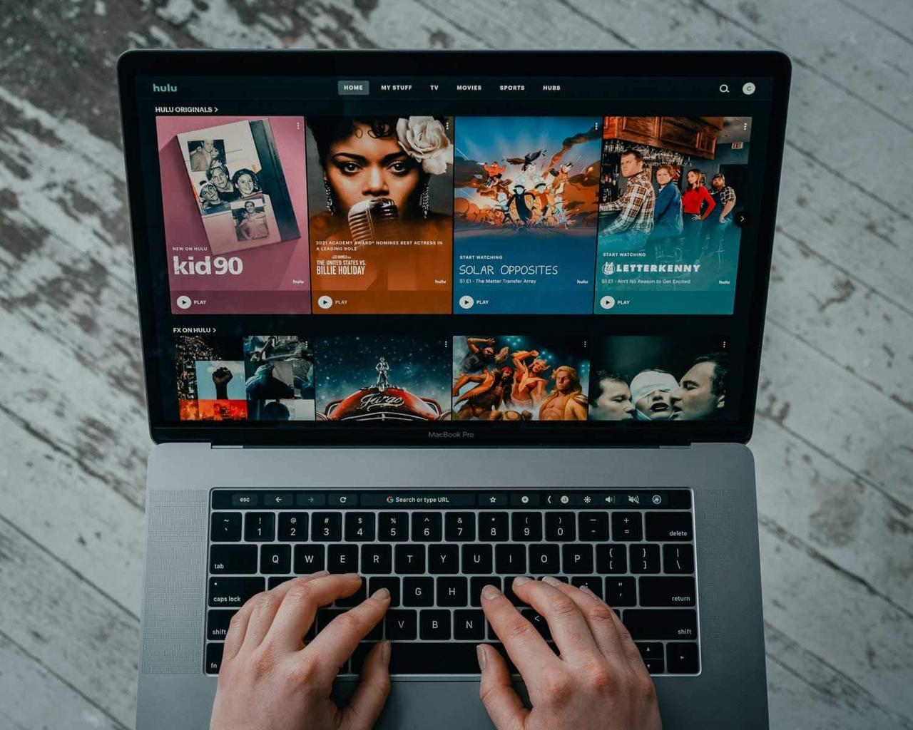 Hände auf der Tastatur eines Laptops, auf dem Bildschirm die Startseite eines Video-Streaming-Dienstes