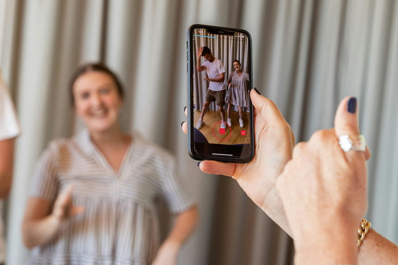 Eine Frau filmt mit dem Smartphone zwei tanzende Kollegen für ein Social-Media-Video