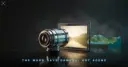 A camera lens aimed at a lit glass panel with the real landscape model standing behind it