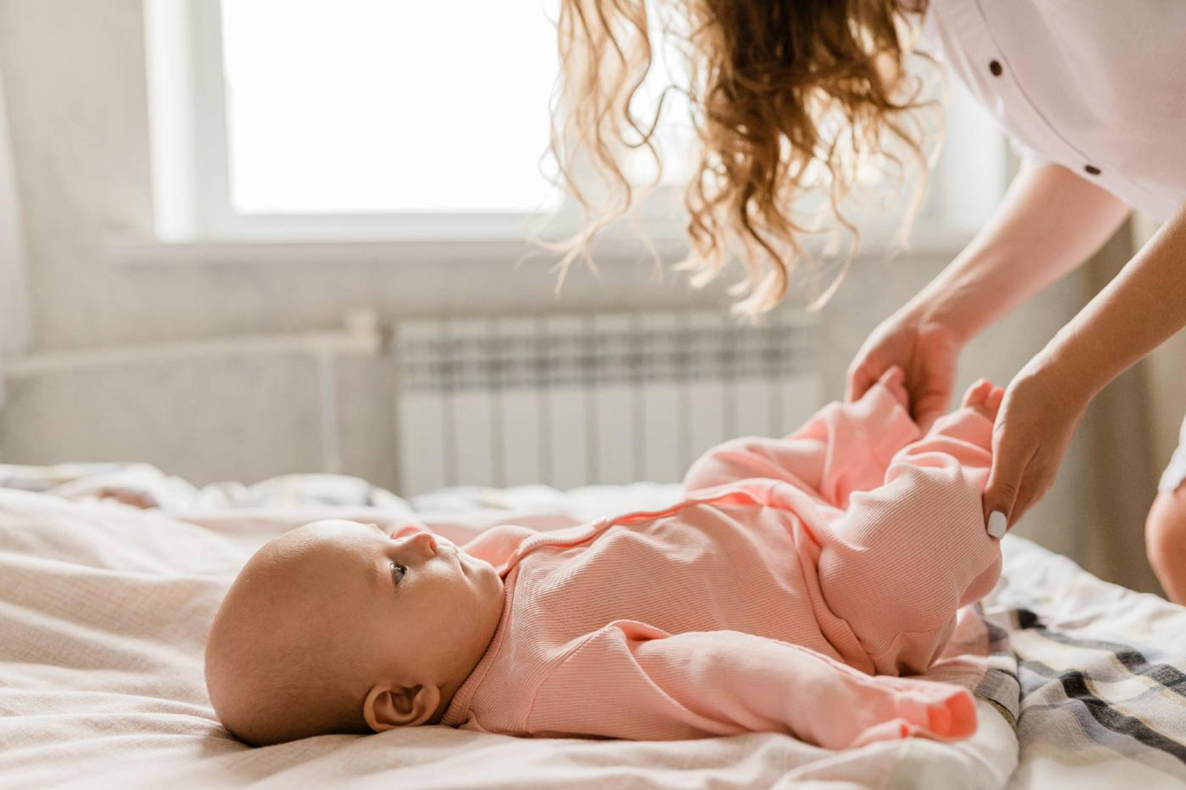 A mother dresses her newborn baby in a pink bodysuit