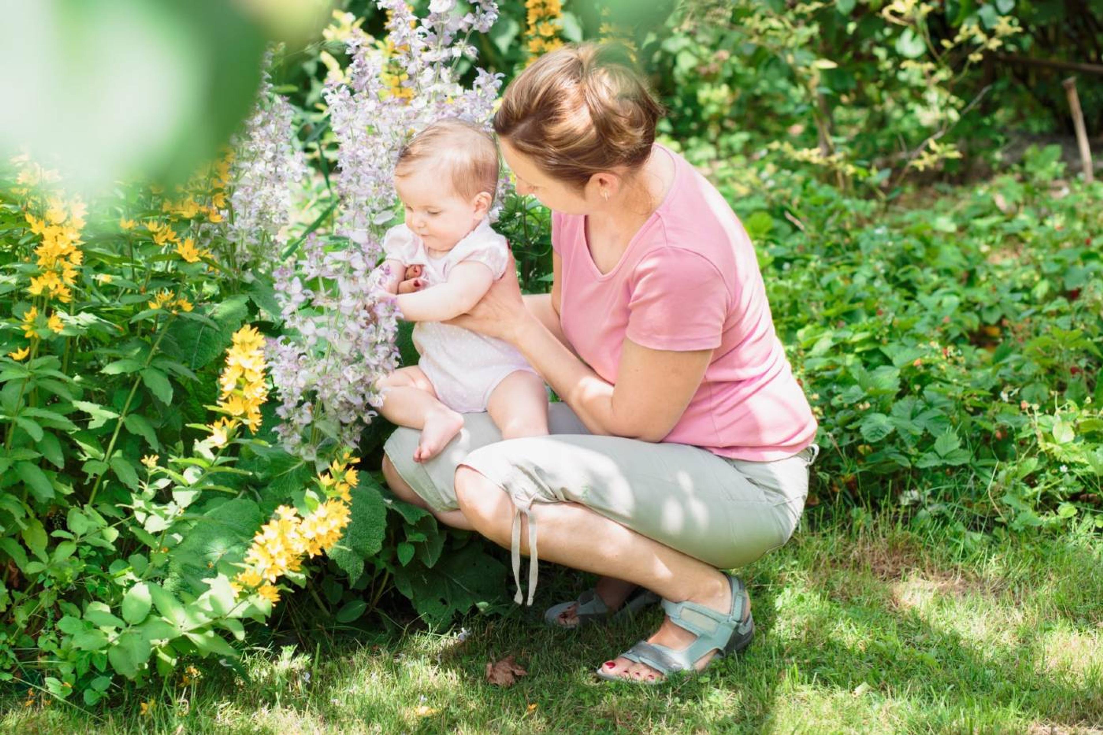 Woman kneeling in garden enjoying nature with baby on her lap