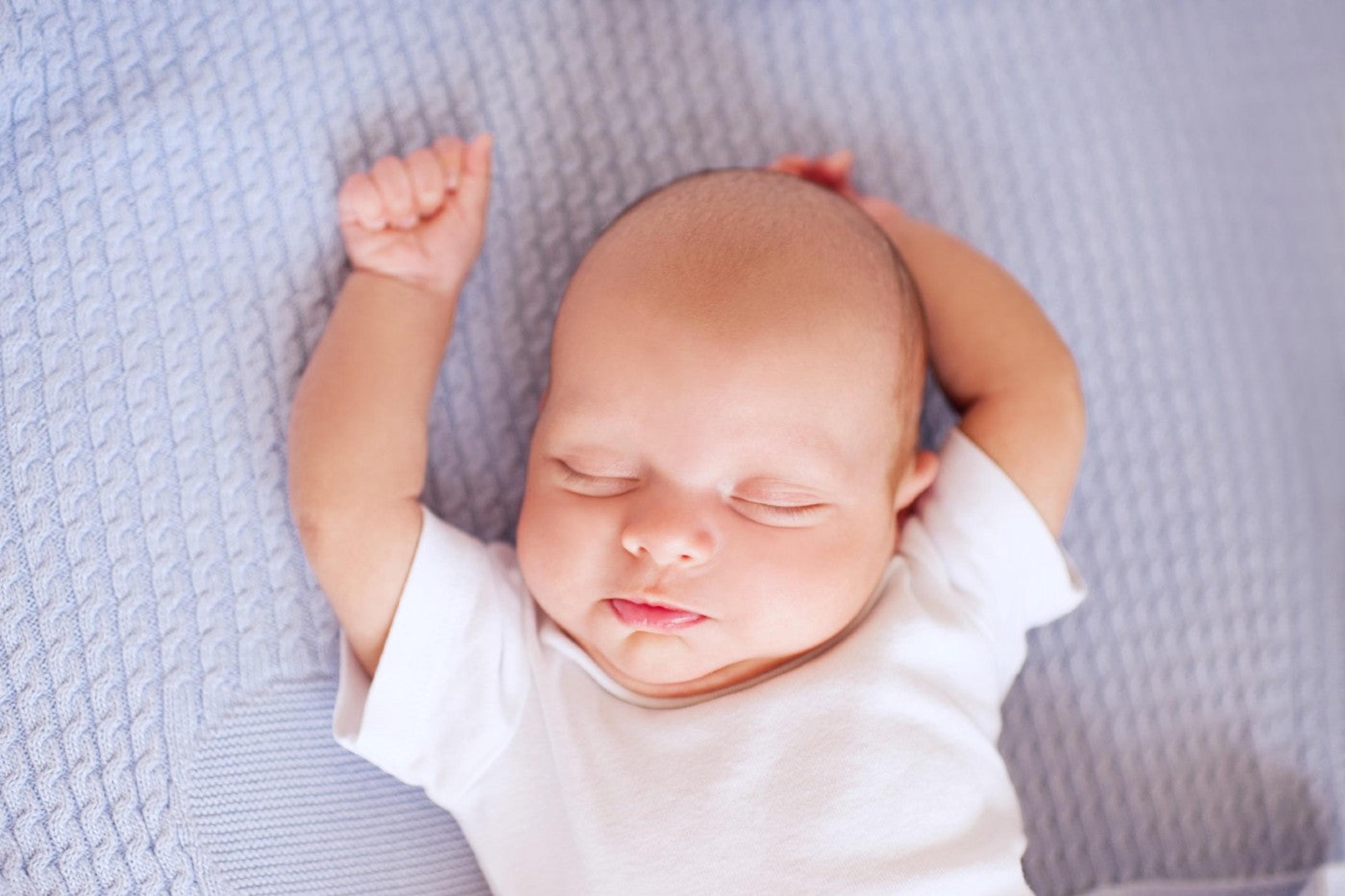 A newborn baby sleeps with arms overhead