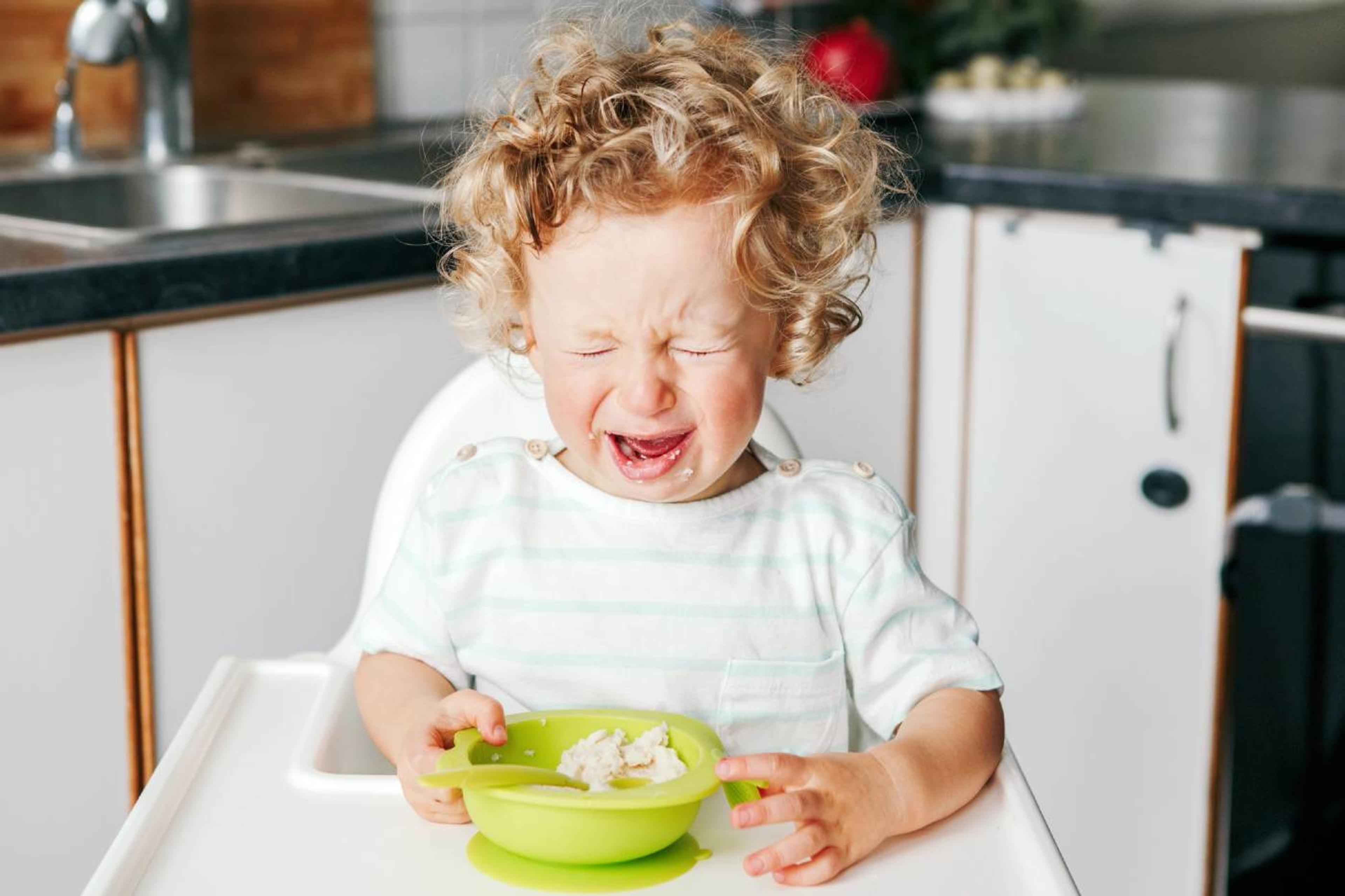 Toddler having a tantrum while sitting in a high chair.