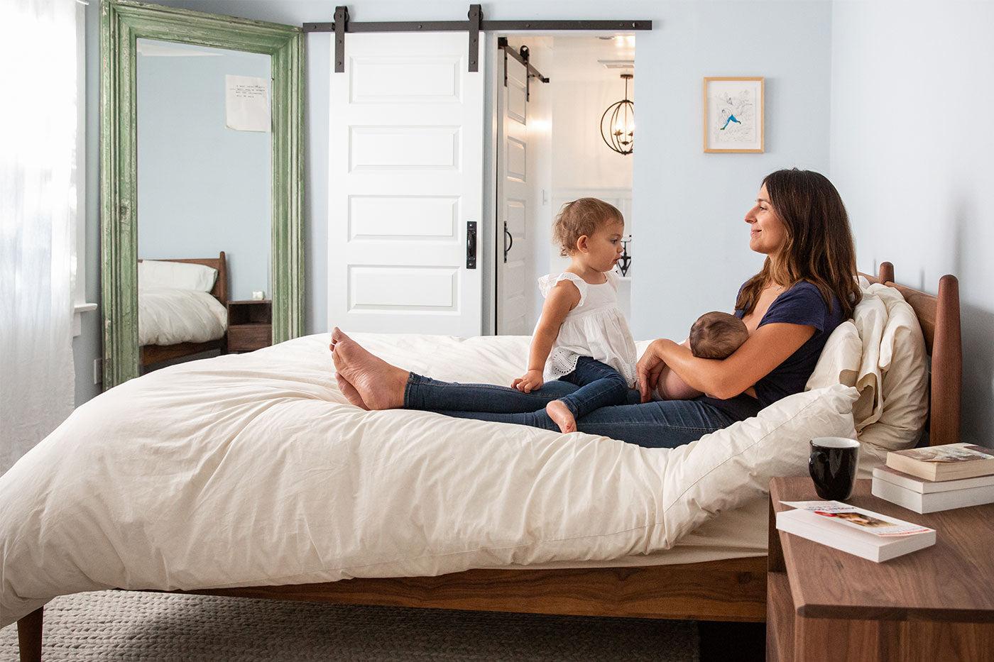 new mother breastfeeding newborn with toddler big sister on bed