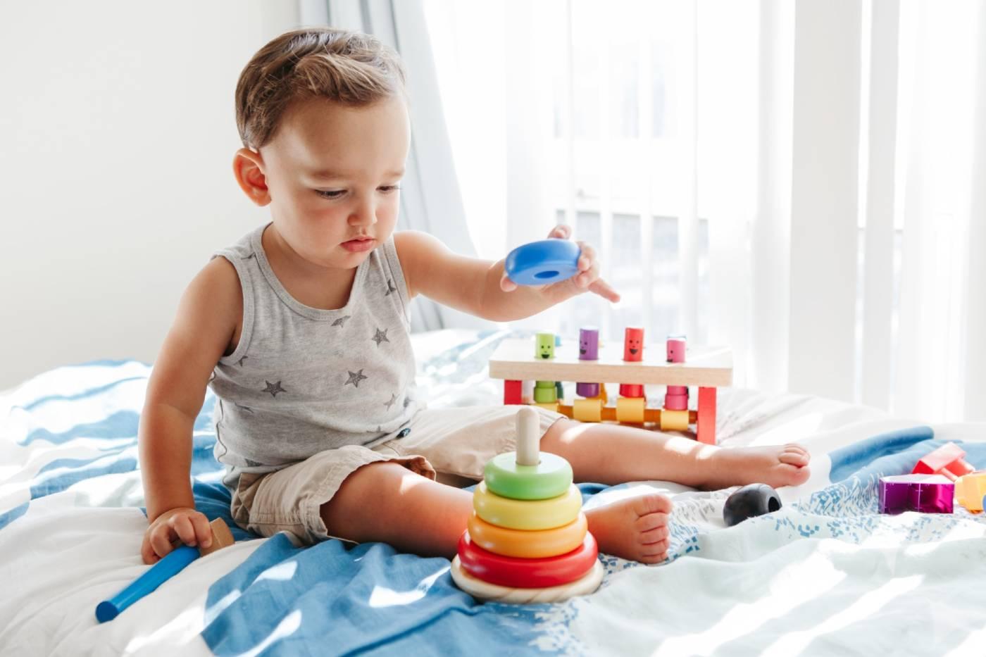 Toddler playing with stacking rings on a bed