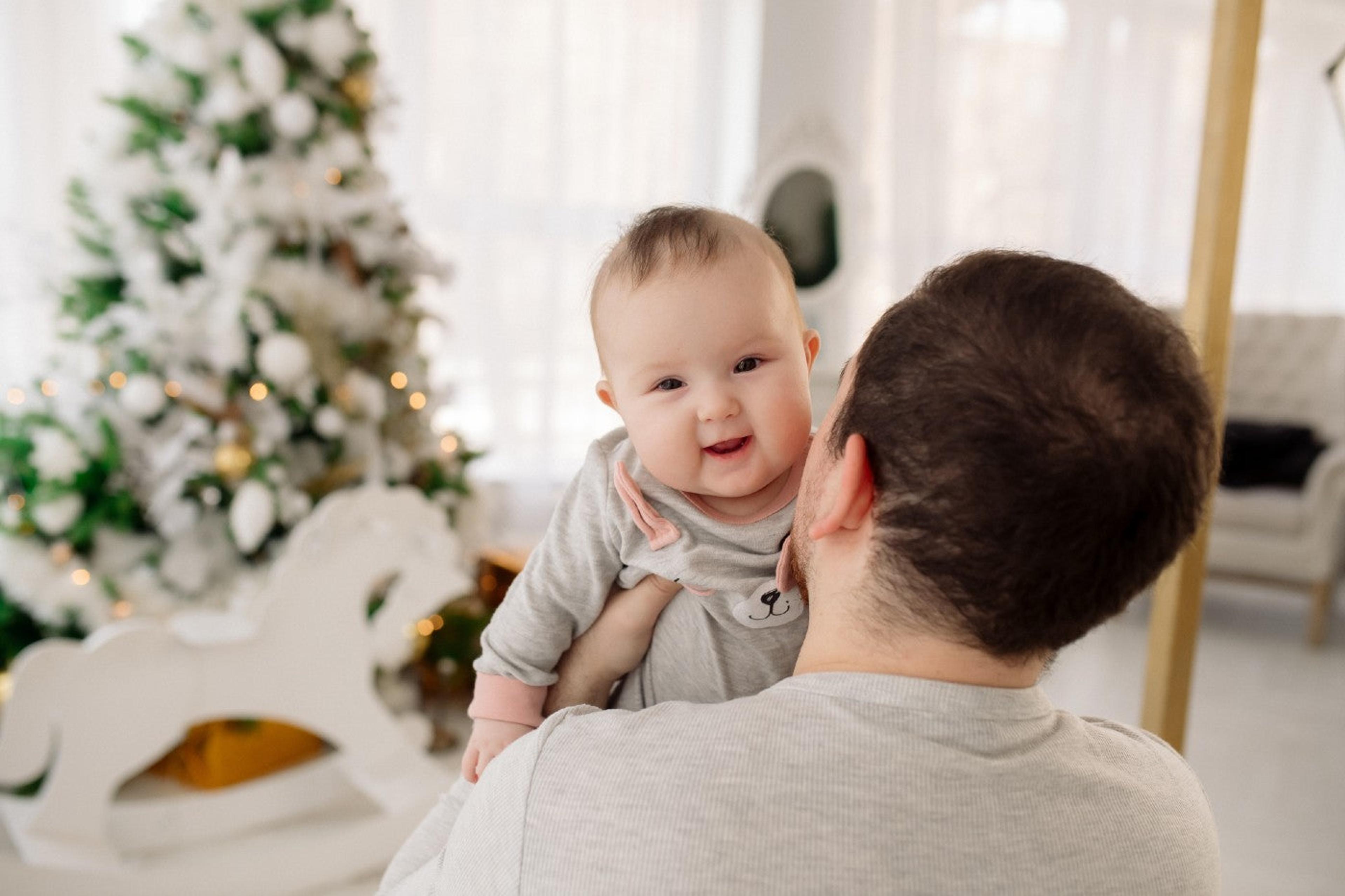 A dad holds his baby near a Christmas tree to celebrate first holiday season