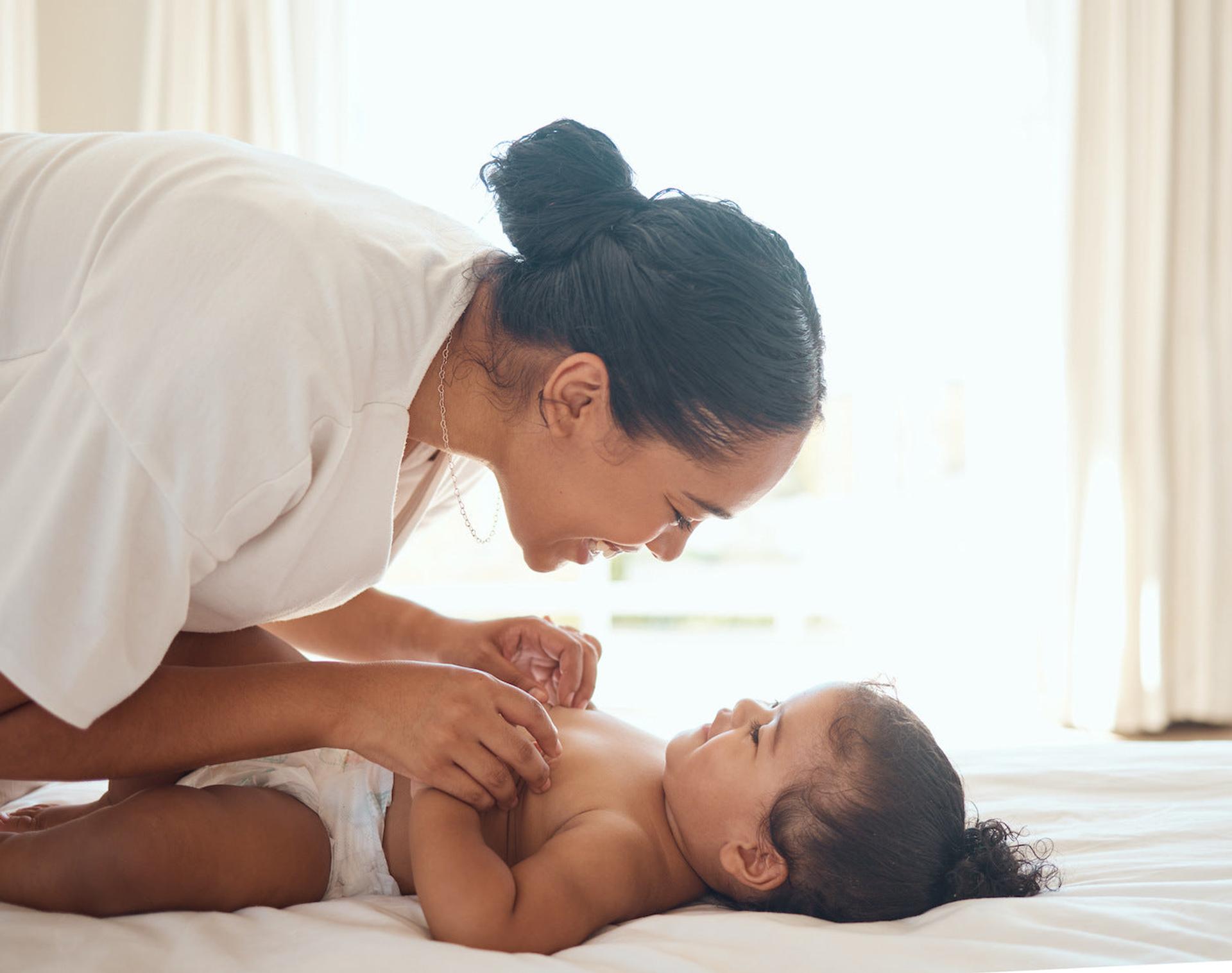 A mom smiles at her baby in a light, bright room