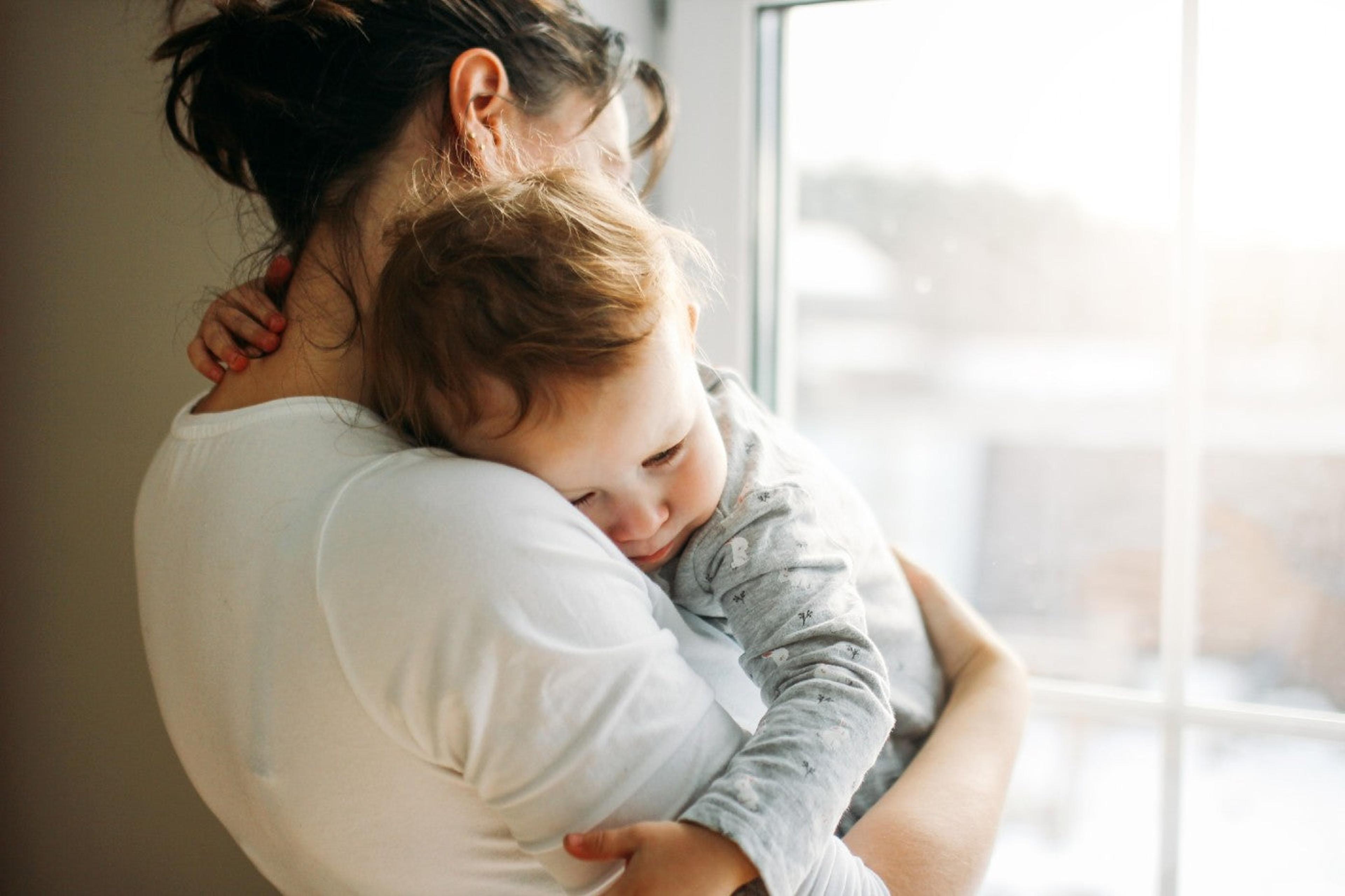 A mom holds her toddler son as she stares out a window