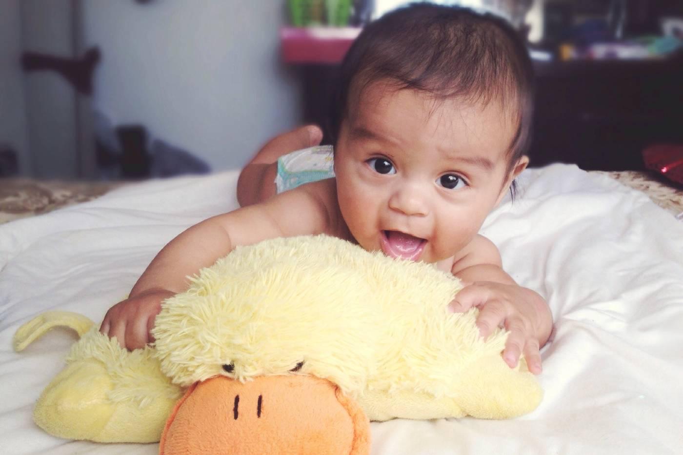 Baby laying on a plush duck pillow on a bed