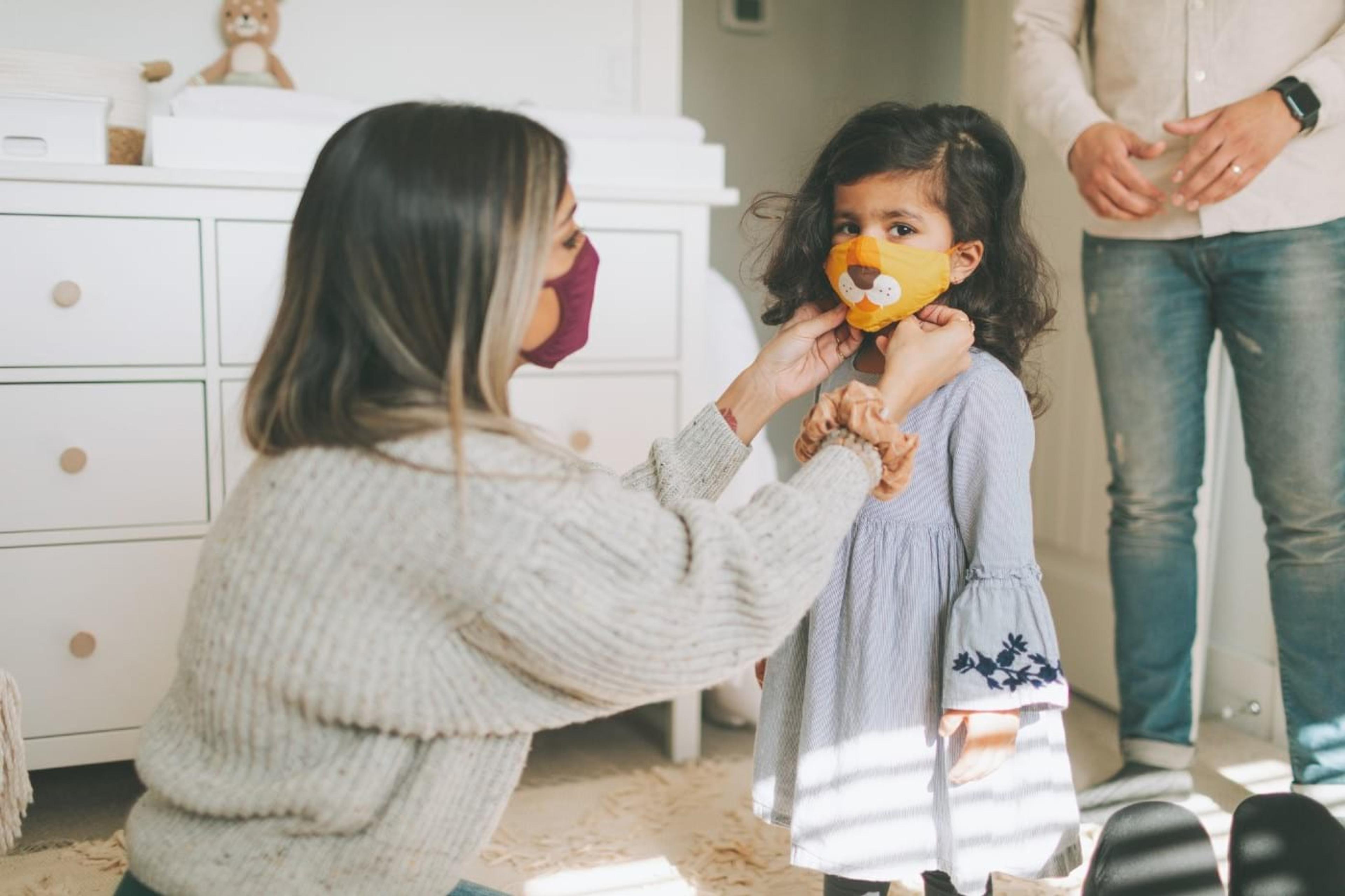 A mother adjusts her daughter's face mask.