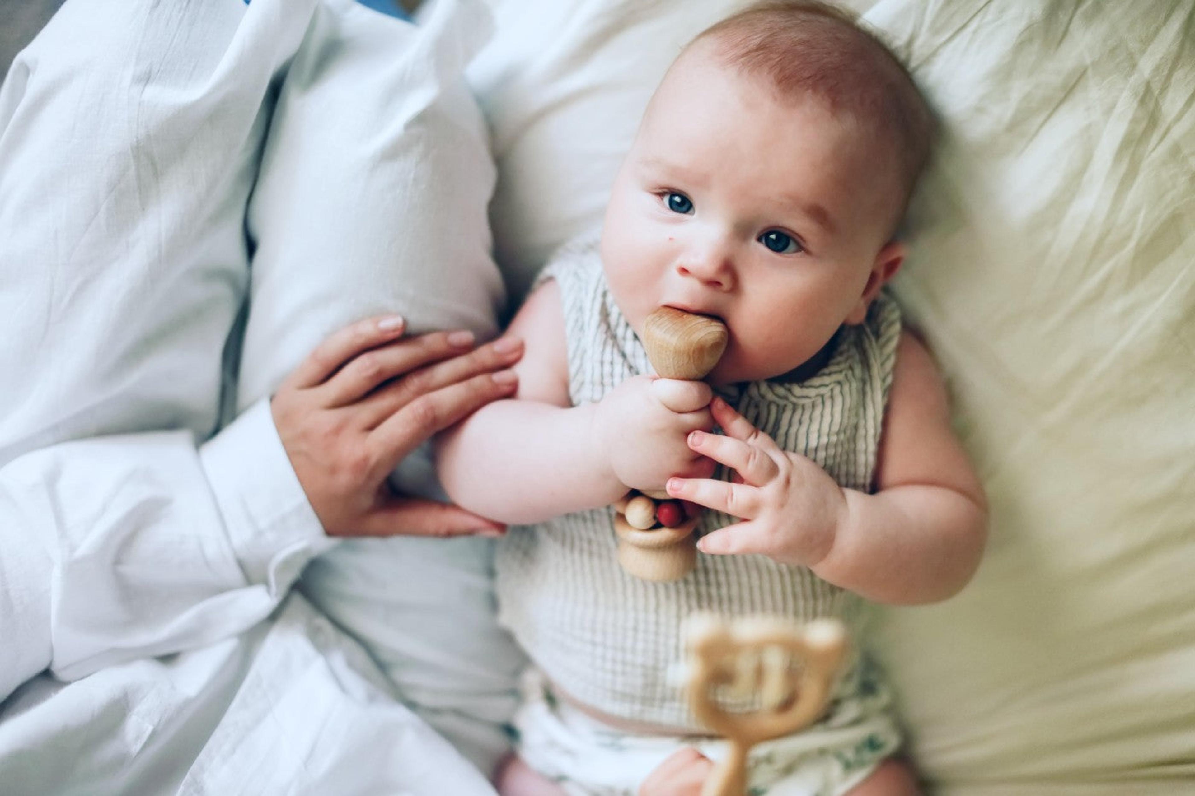 3-month-old baby chews on a wooden rattle toy
