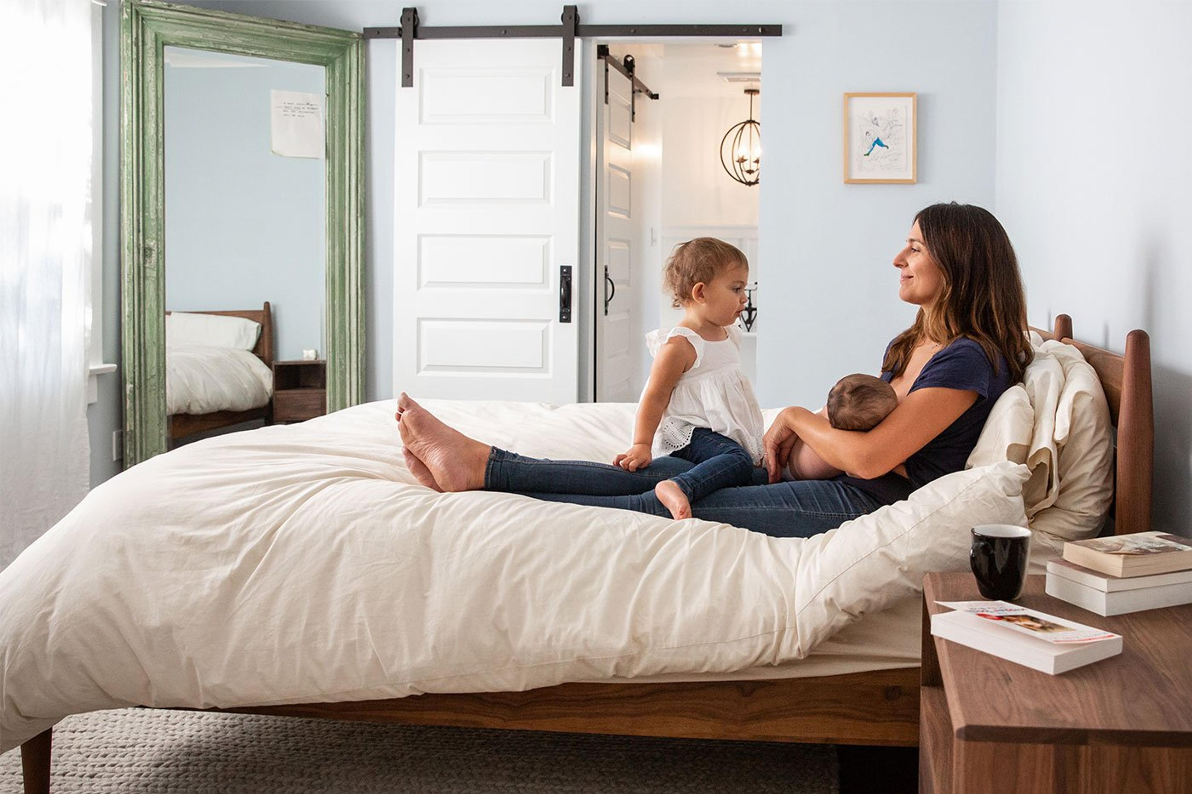 new mother breastfeeding newborn with toddler big sister on bed