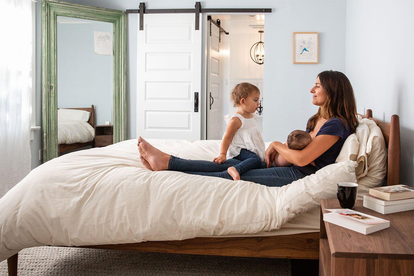 new mother breastfeeding newborn with toddler big sister on bed