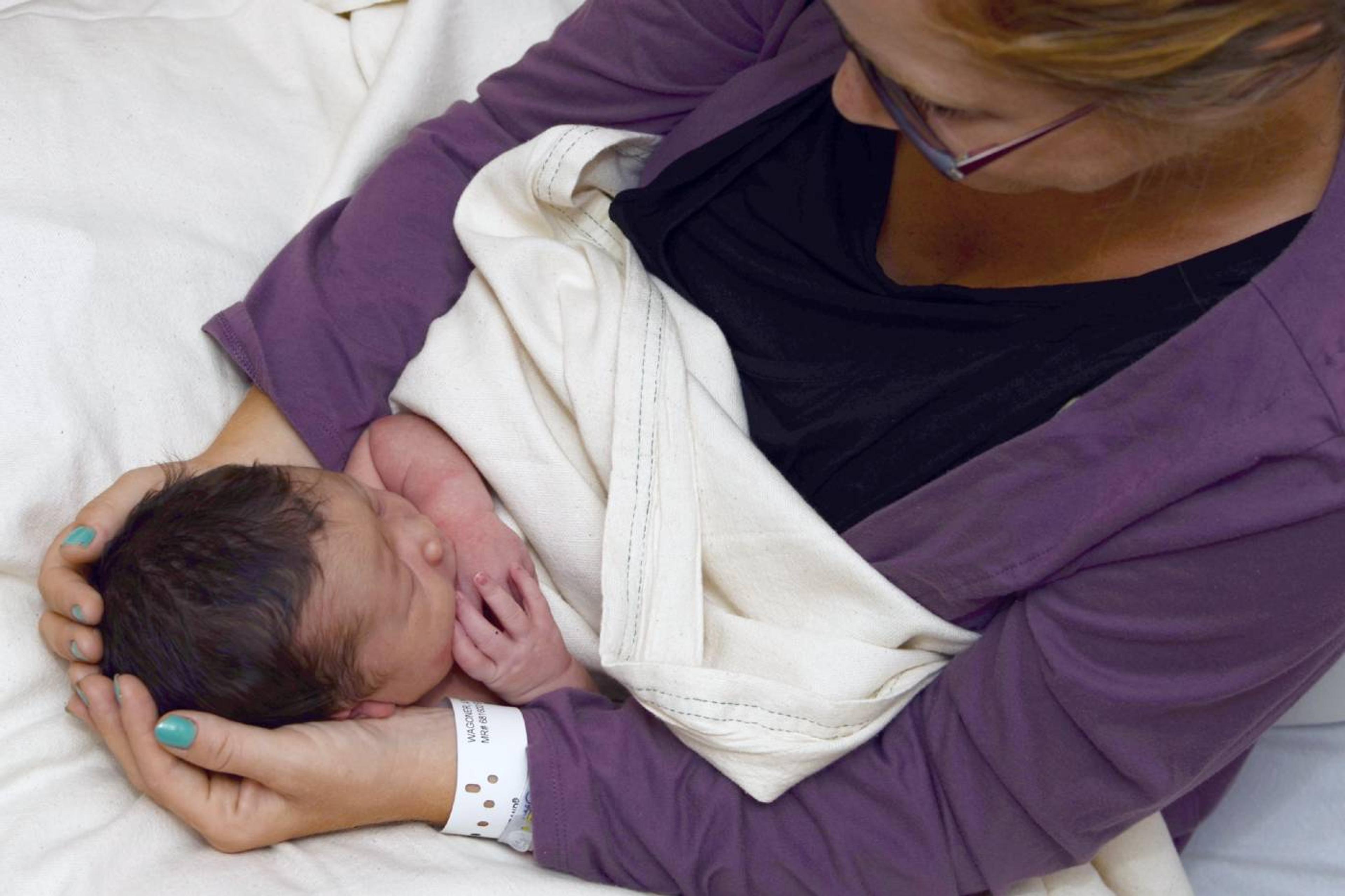 A new mom cradles her newborn baby, who has a full head of hair.