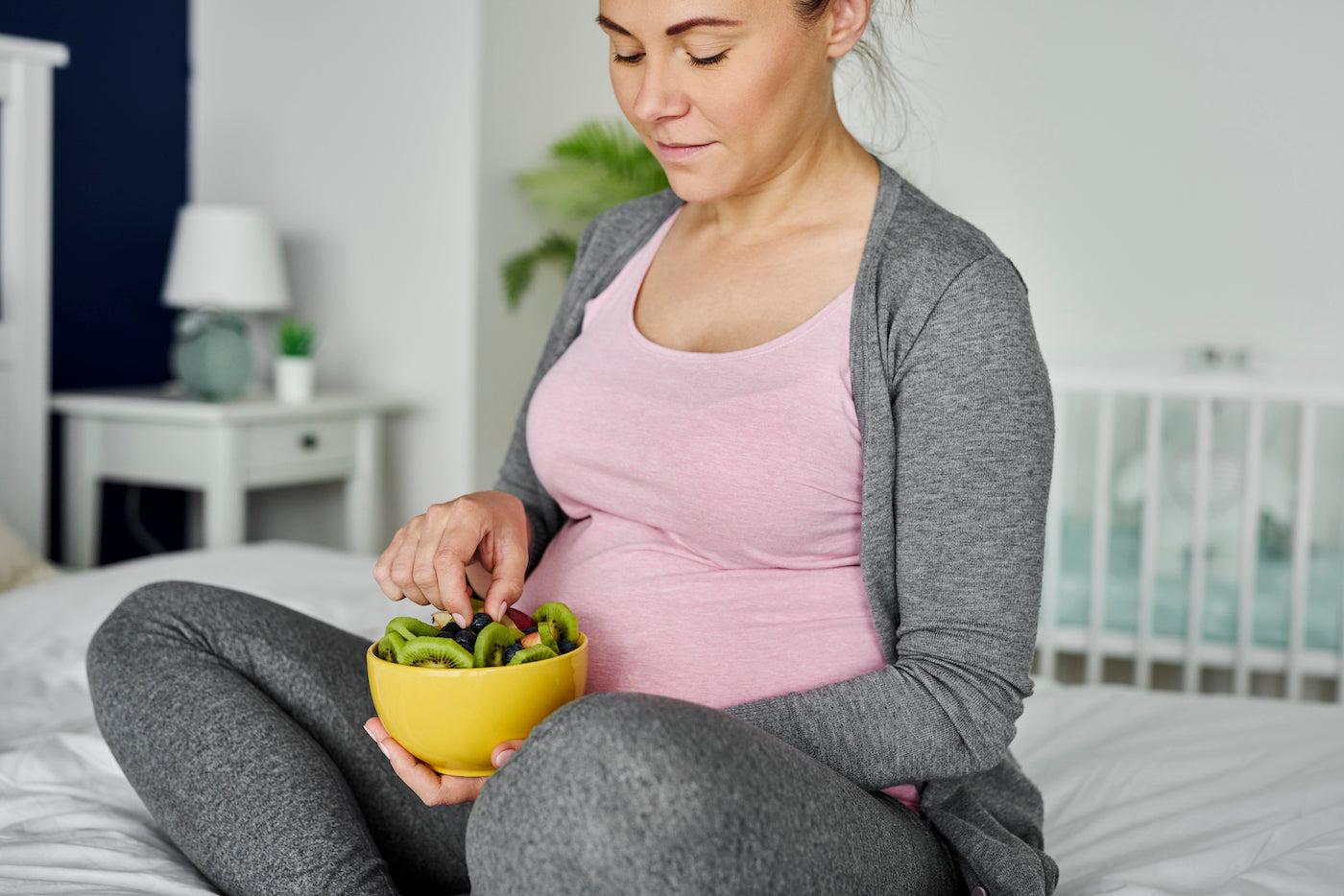 A pregnant woman snacks on a bowl of fruit to satisfy a pregnancy craving