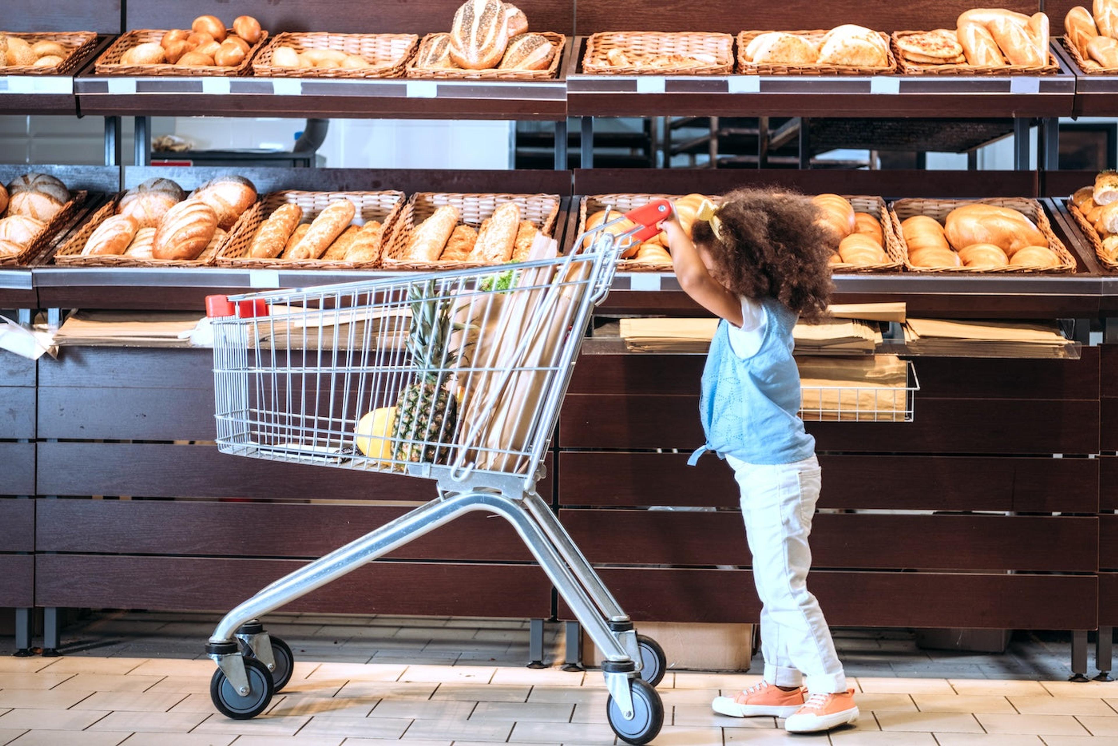 A toddler pushes a grocery cart in the bread aisle
