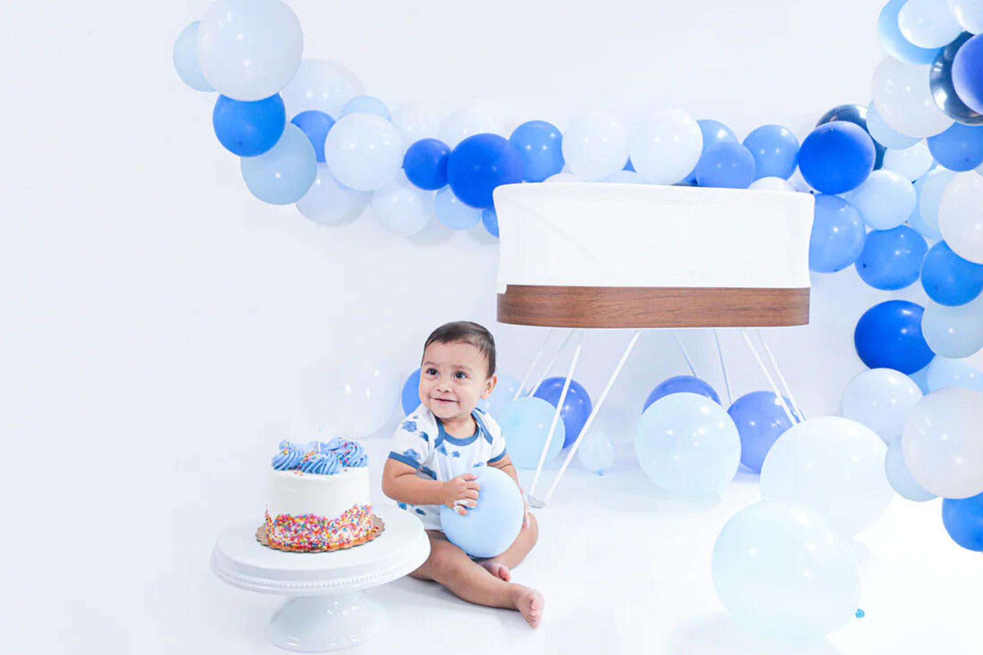 Toddler sitting on floor with birthday cake, SNOO, and balloons