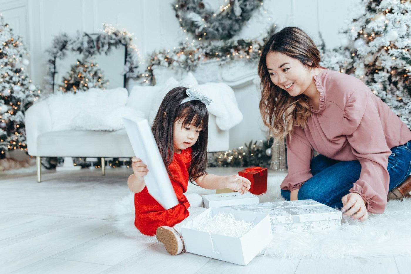 Toddler girl unwraps a Christmas gift as her mother watches