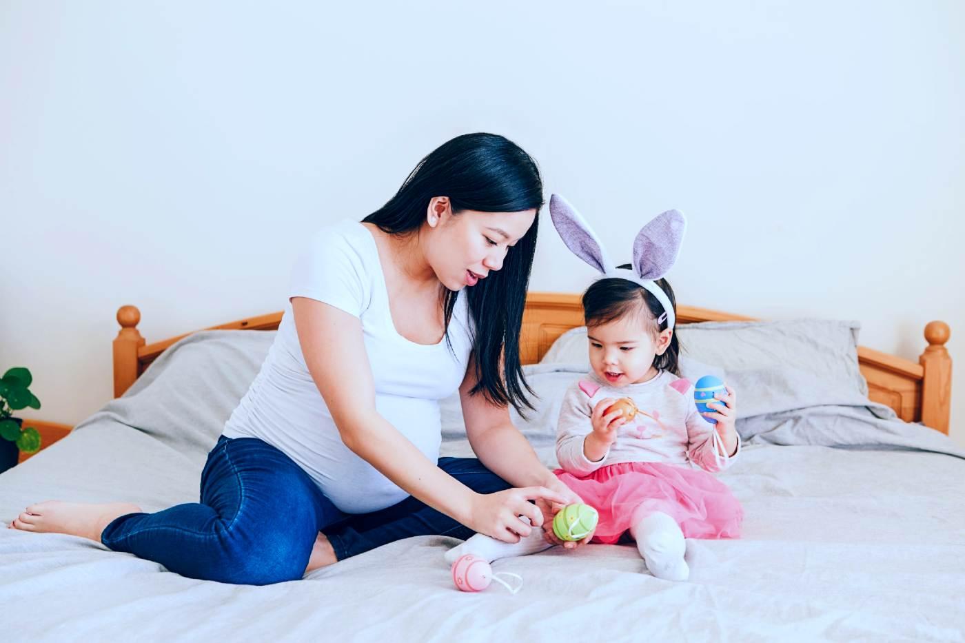 Easter activities for toddlers - pregnant mom and toddler playing with Easter eggs on a bed