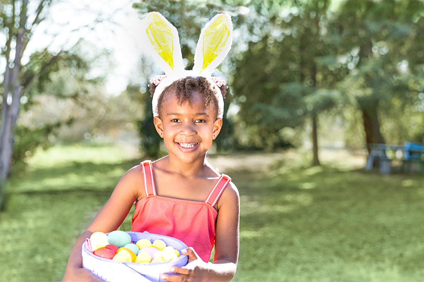 Easter basket ideas: Young girl wearing bunny ears and holding basket full of colored eggs