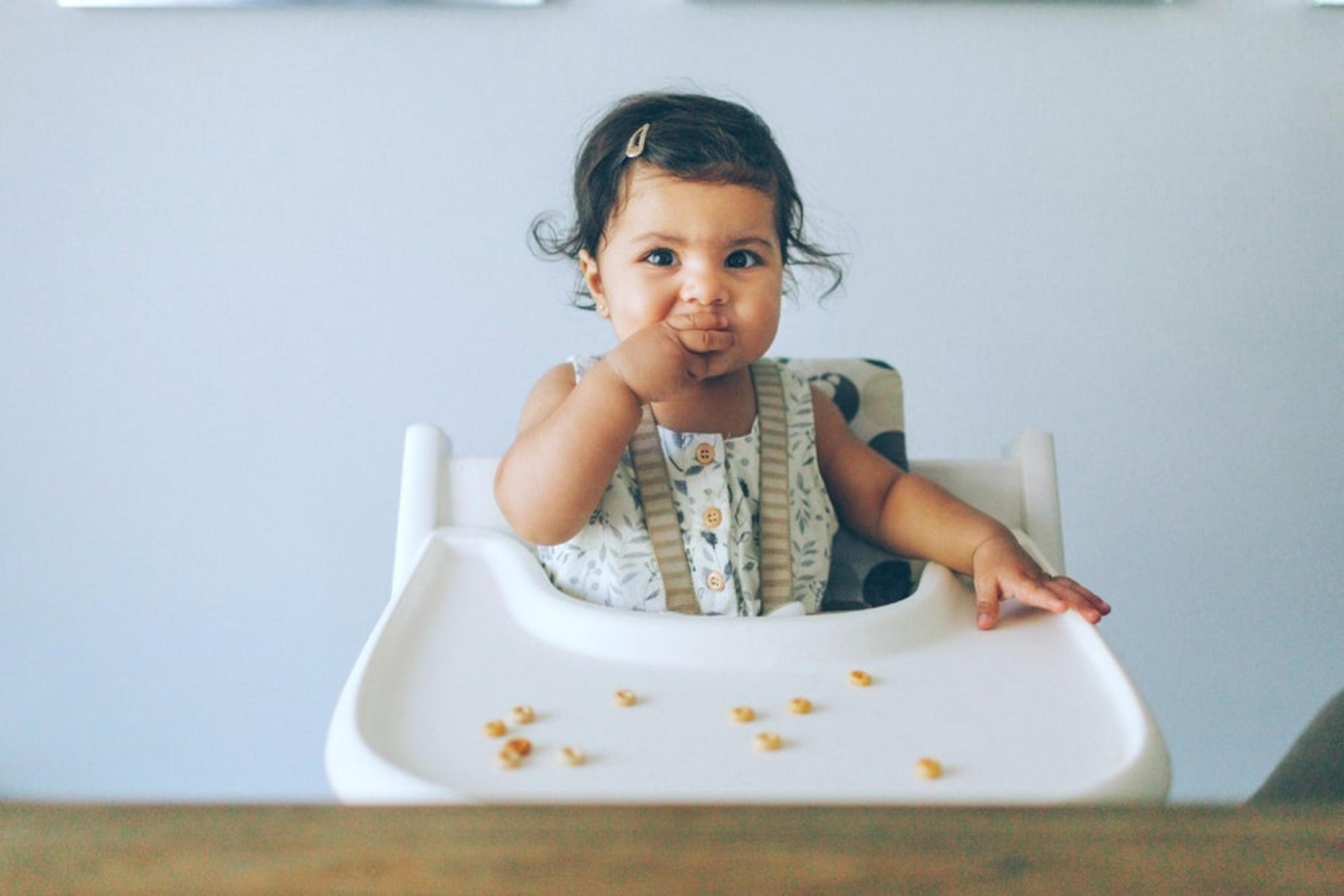 Baby girl eats finger food in a highchair 