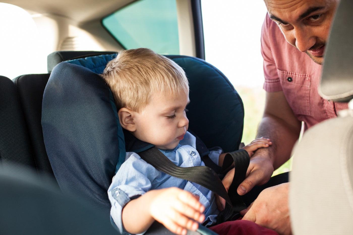 A dad buckles his son into a car seat