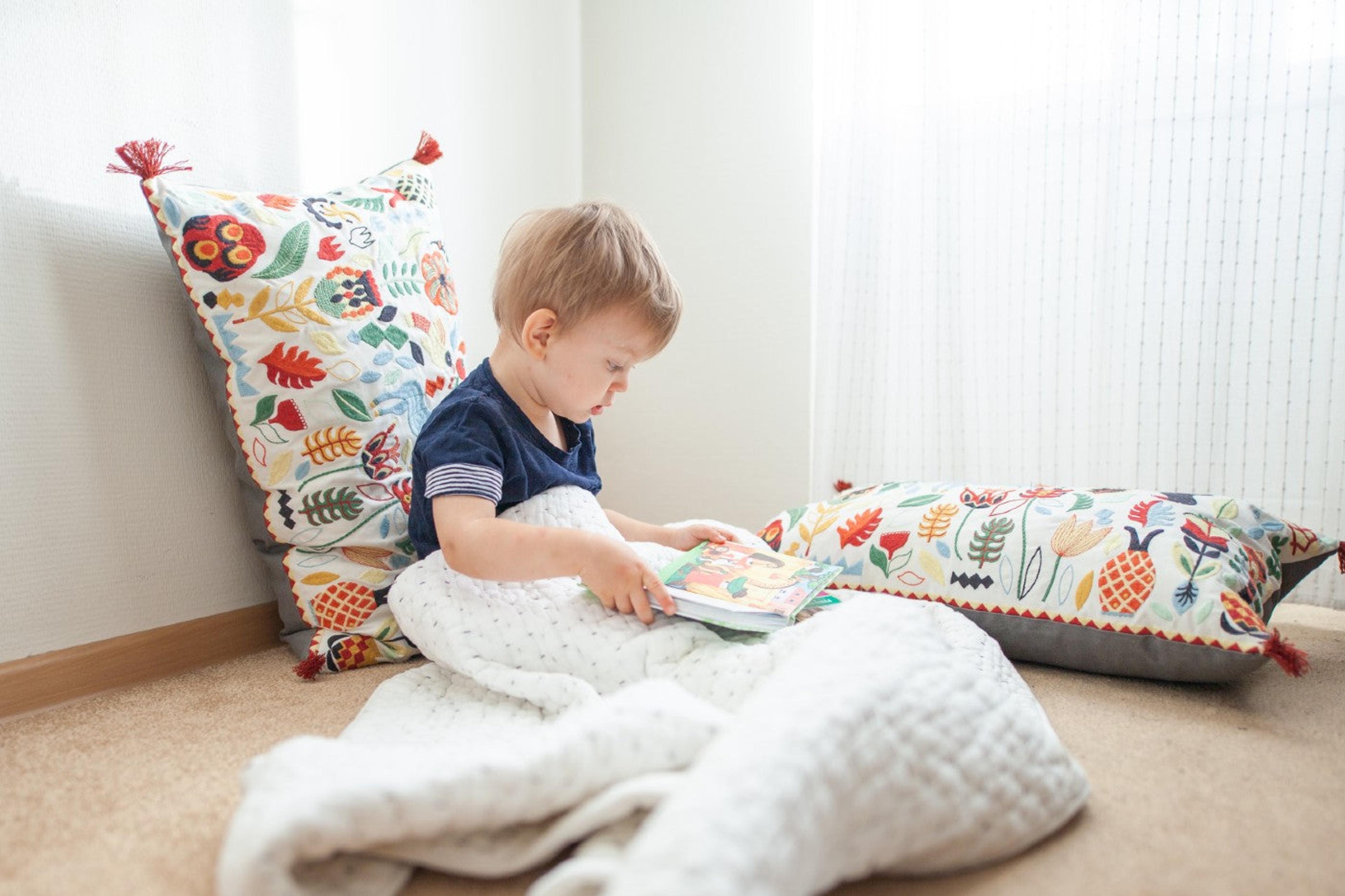 A toddler boy reads a book on the floor