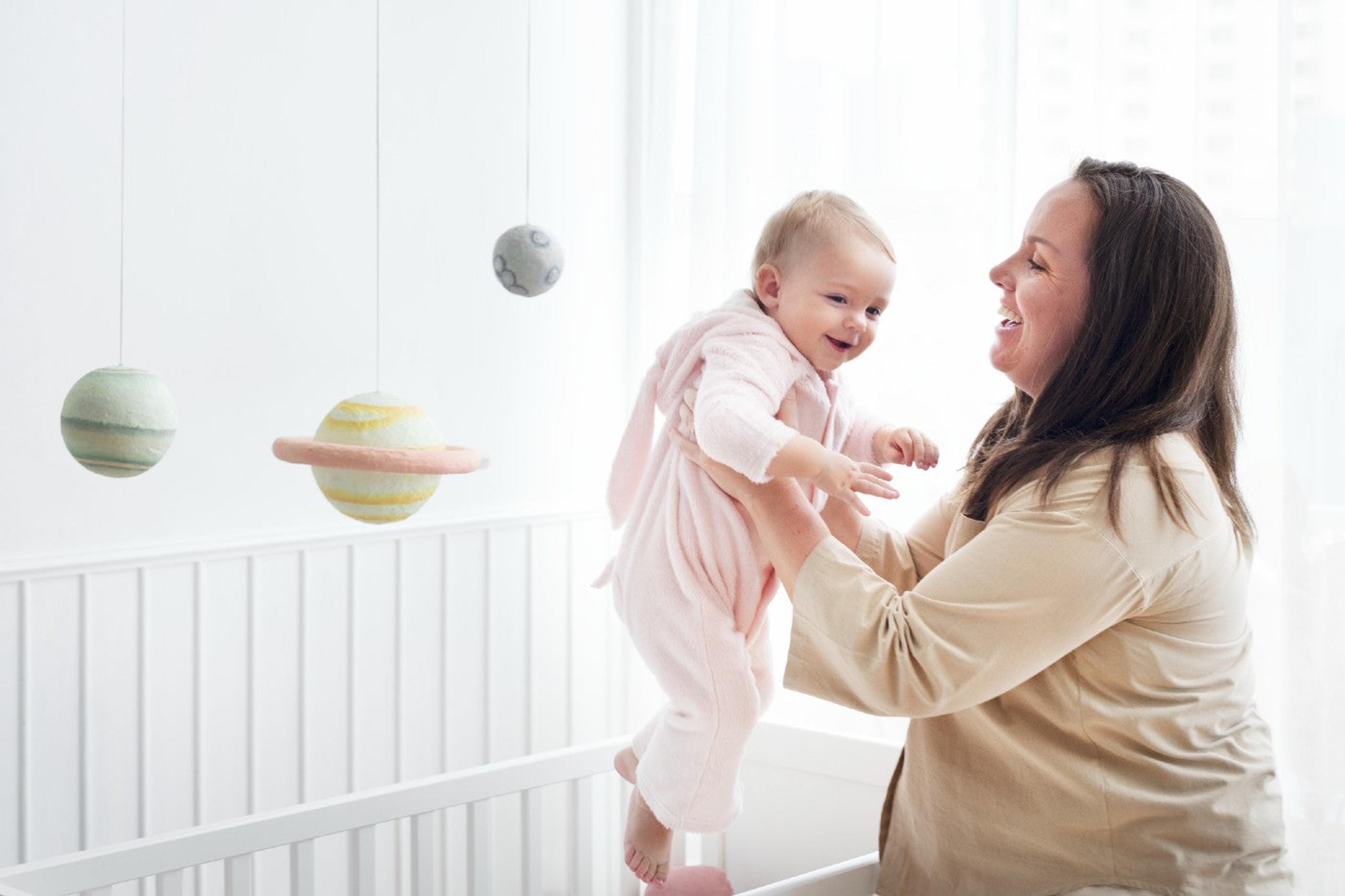 Mom puts baby in crib as planet-themed mobile hangs in the background