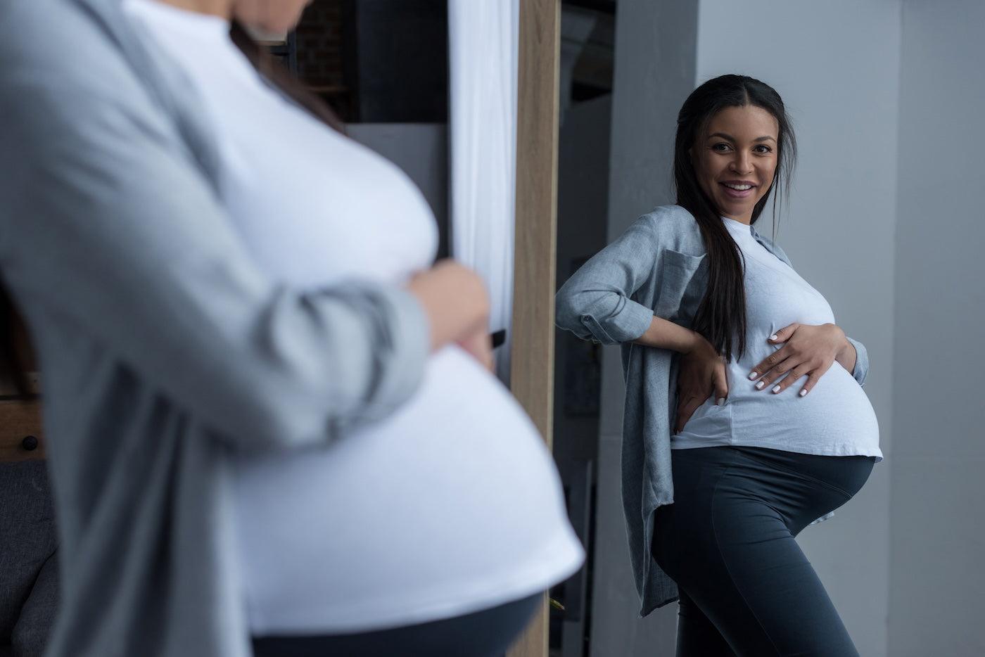 A pregnant woman looks at her baby bump in the mirror