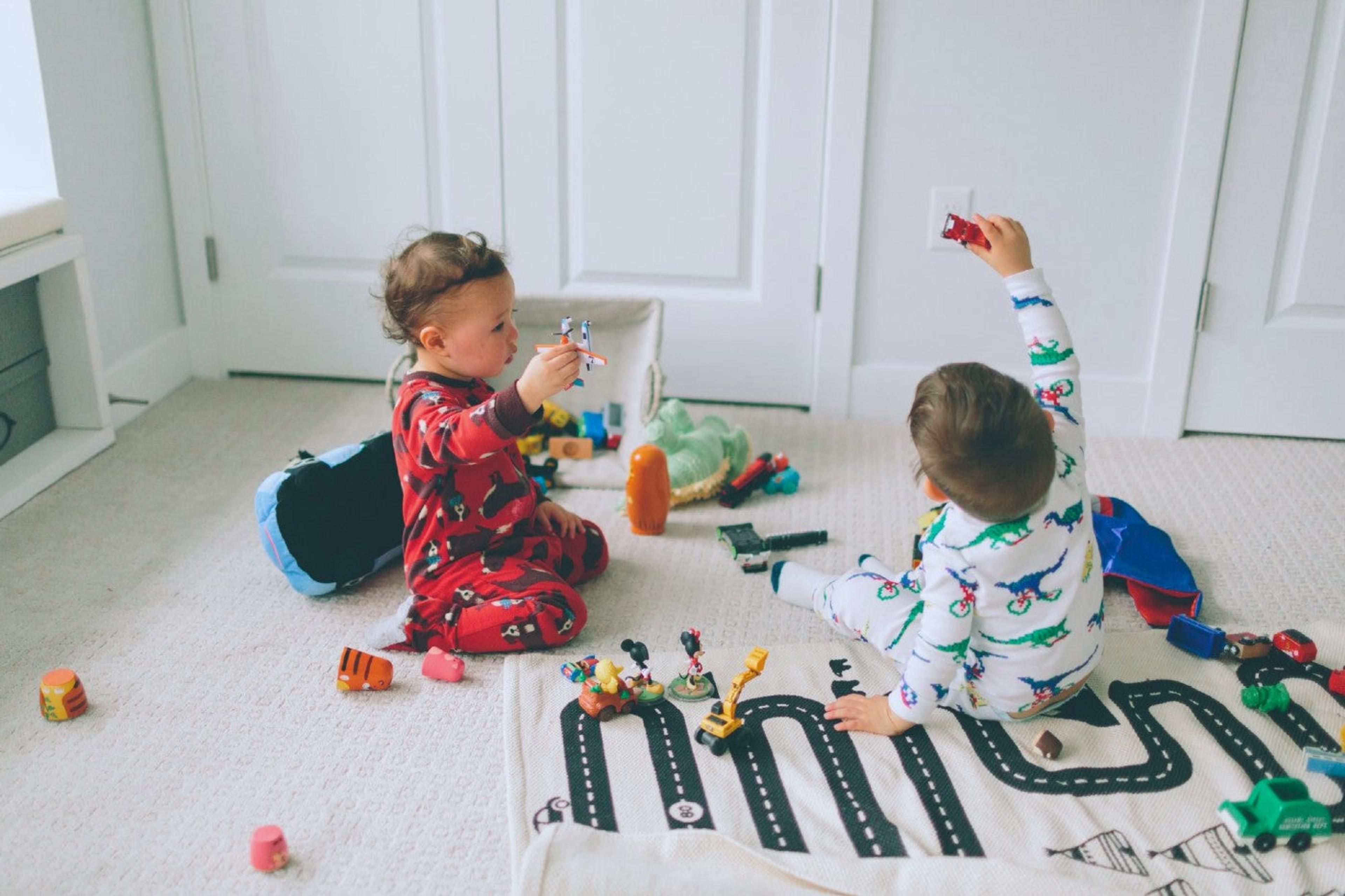 Two toddler boys play on the carpet with cars and a road rug