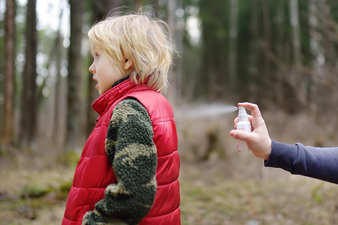 mom sprays mosquito repellant on child's clothes