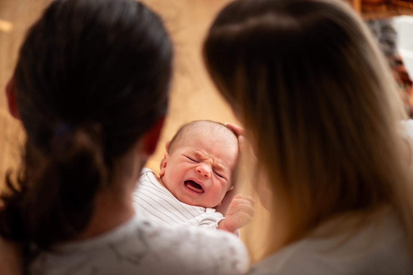 Two women look at a crying newborn baby