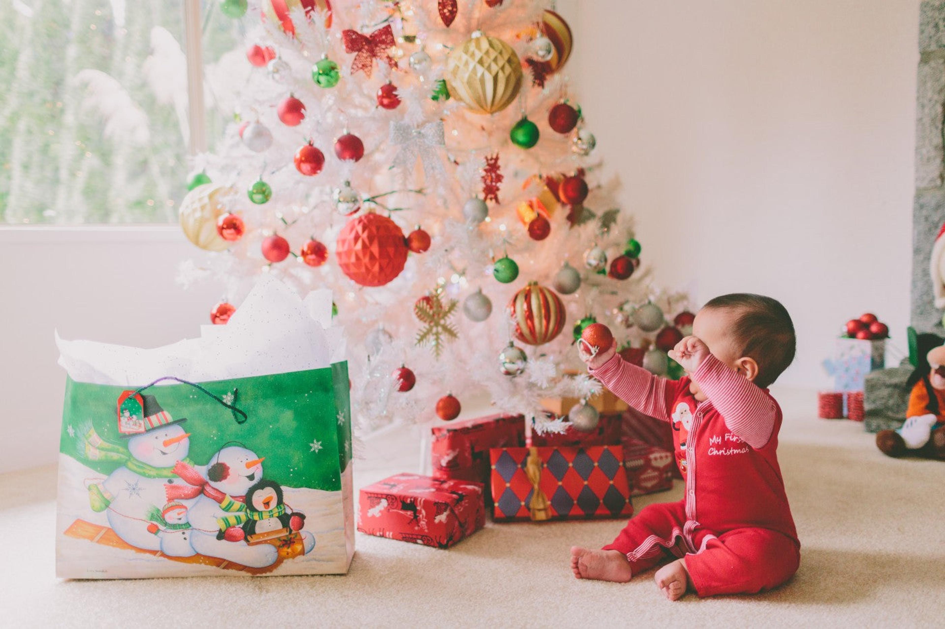 Baby on floor in front of white Christmas tree, celebrating their first holiday