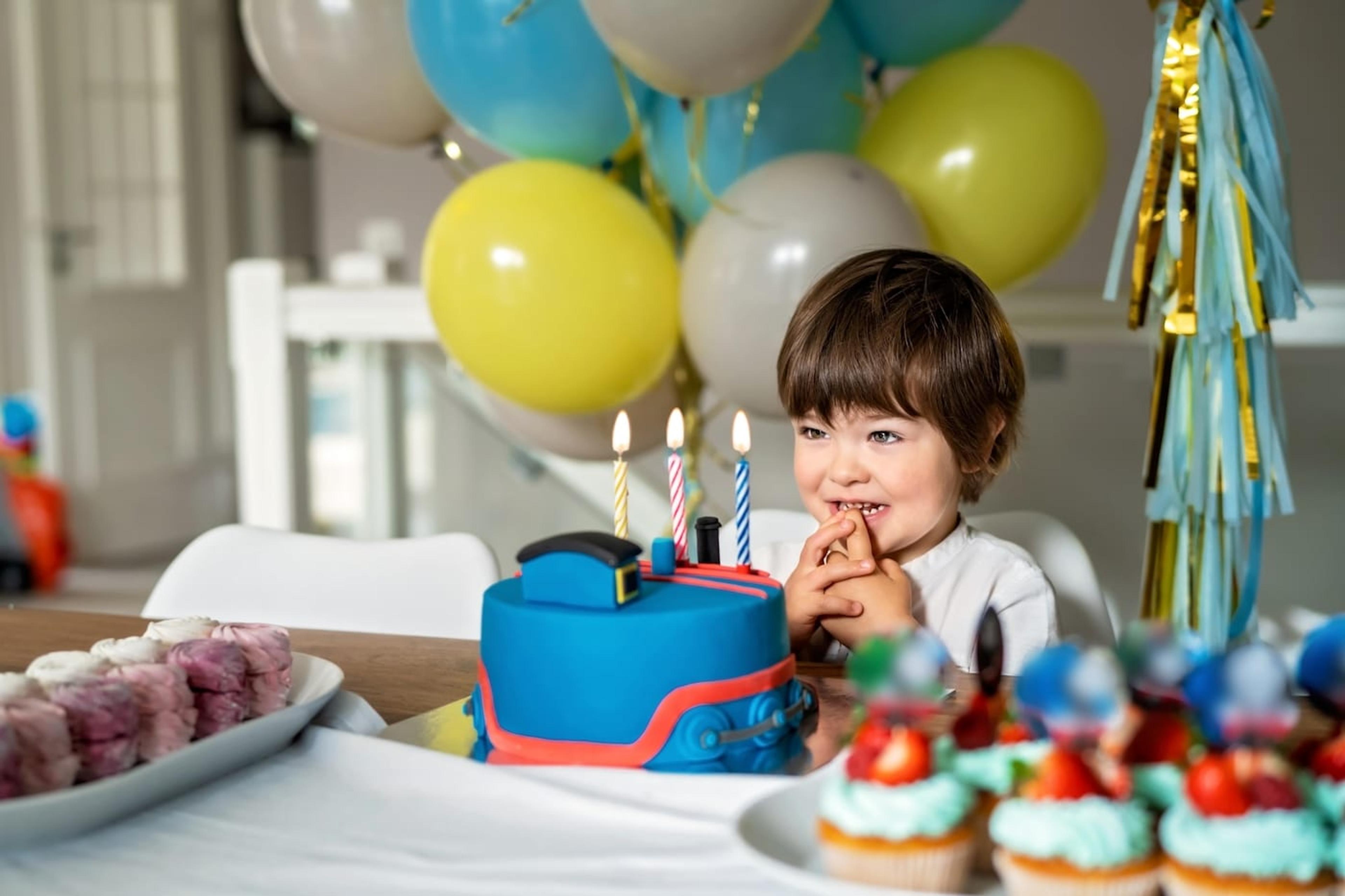 A child celebrates at a train-themed third birthday party