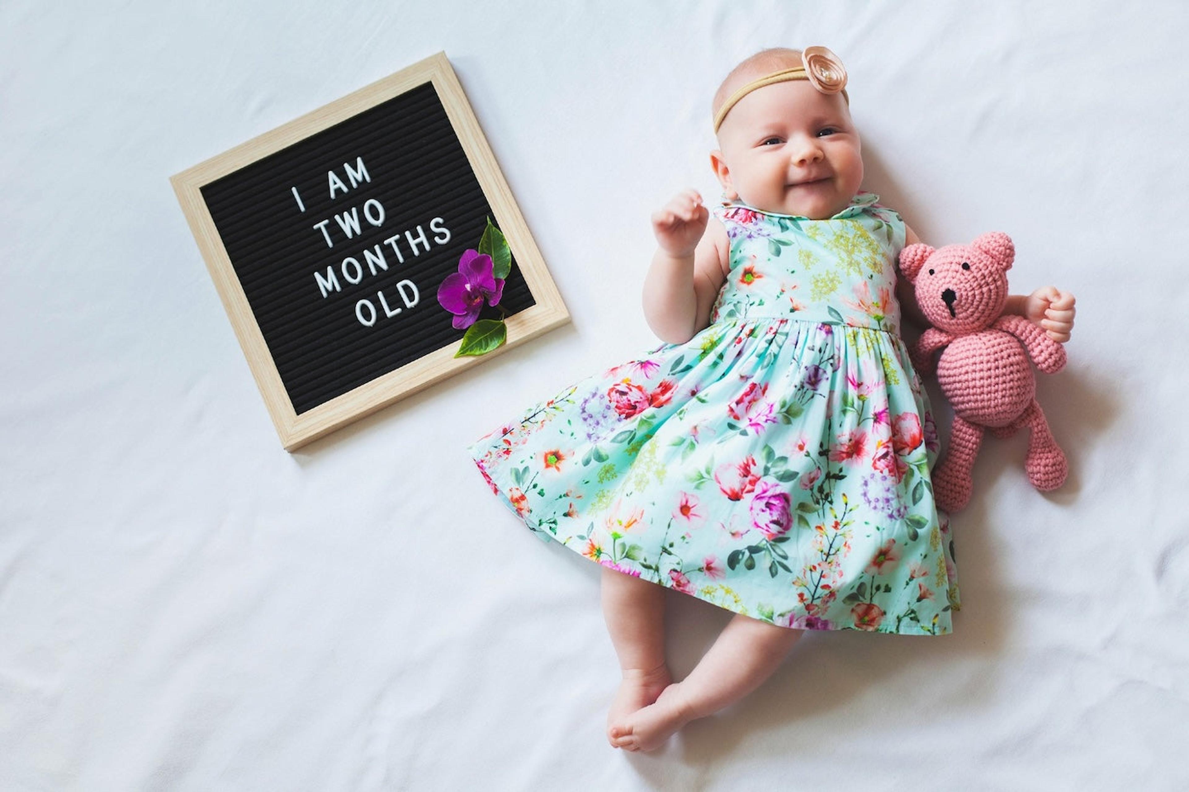 2-month-old baby girl poses with teddy bear and letterboard that says 'I am two months old"