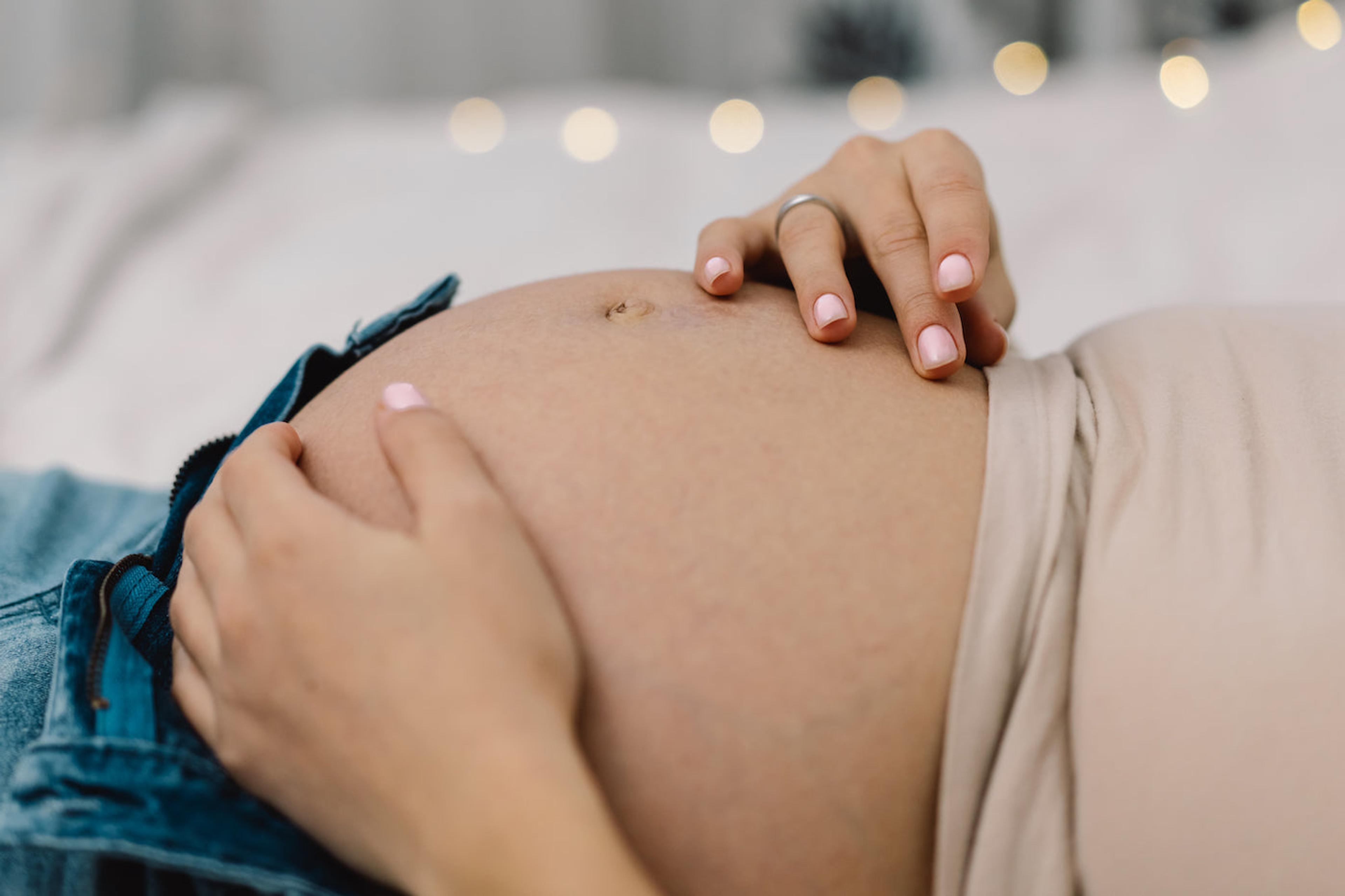 A woman cradles her pregnant belly, contemplating perineal massage