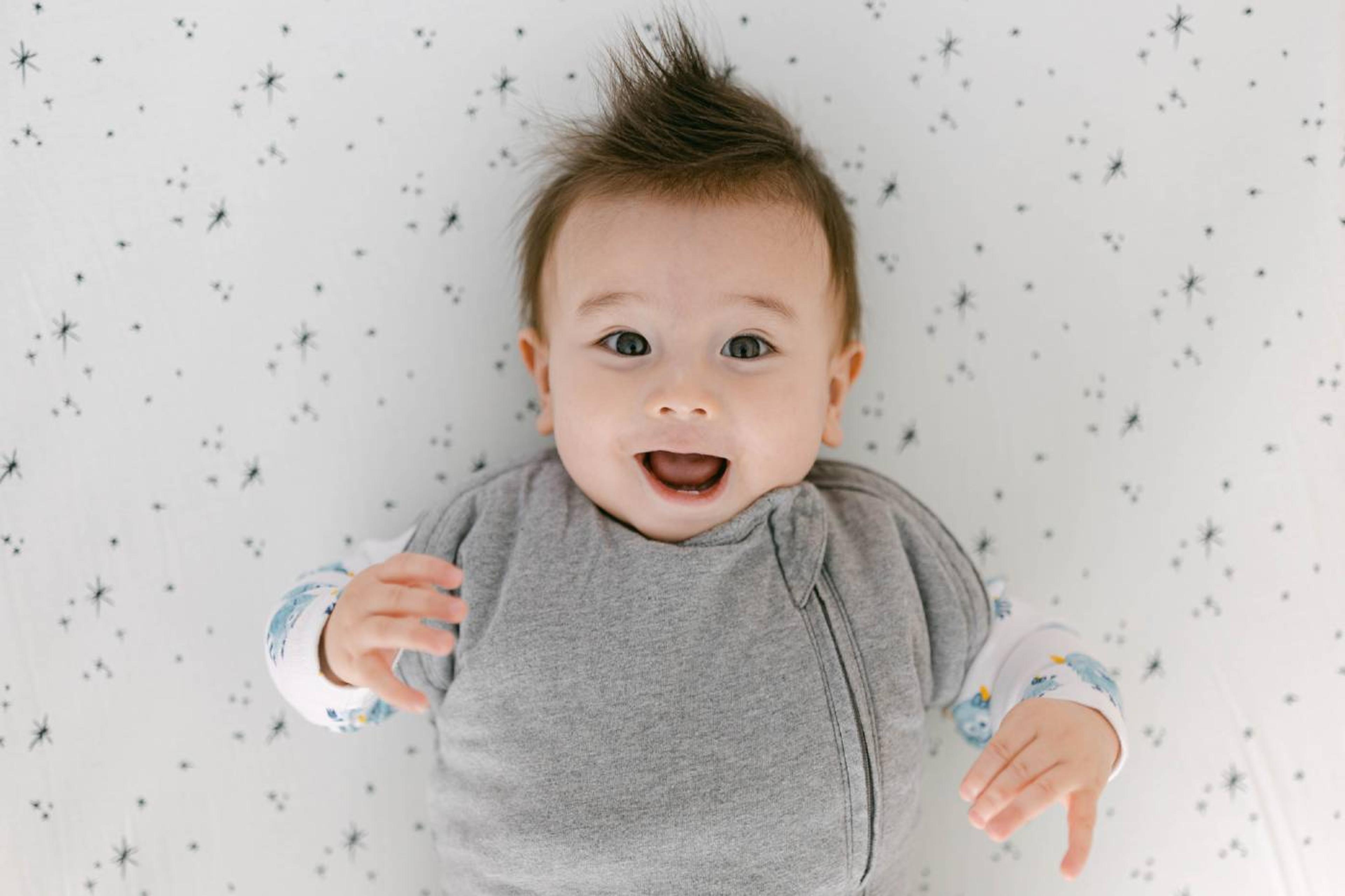 Baby laying on sheet, wearing organic bodysuit and Sleepea