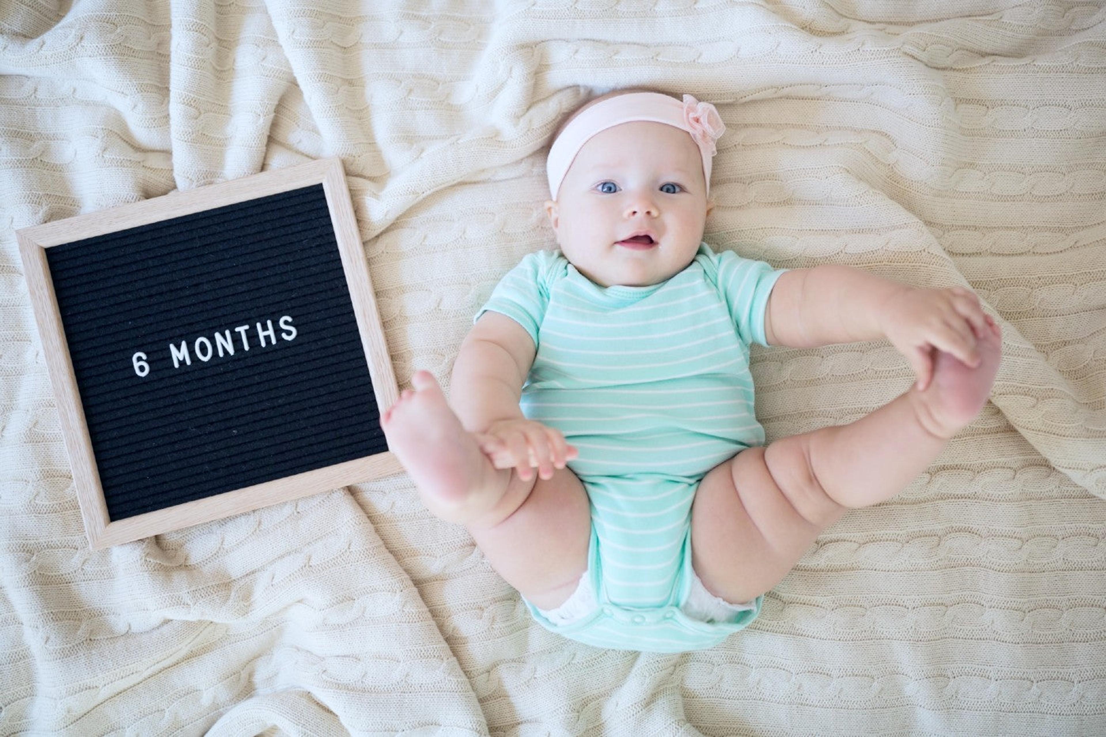 A 6-month-old baby poses next to a letterboard that says "6 months"