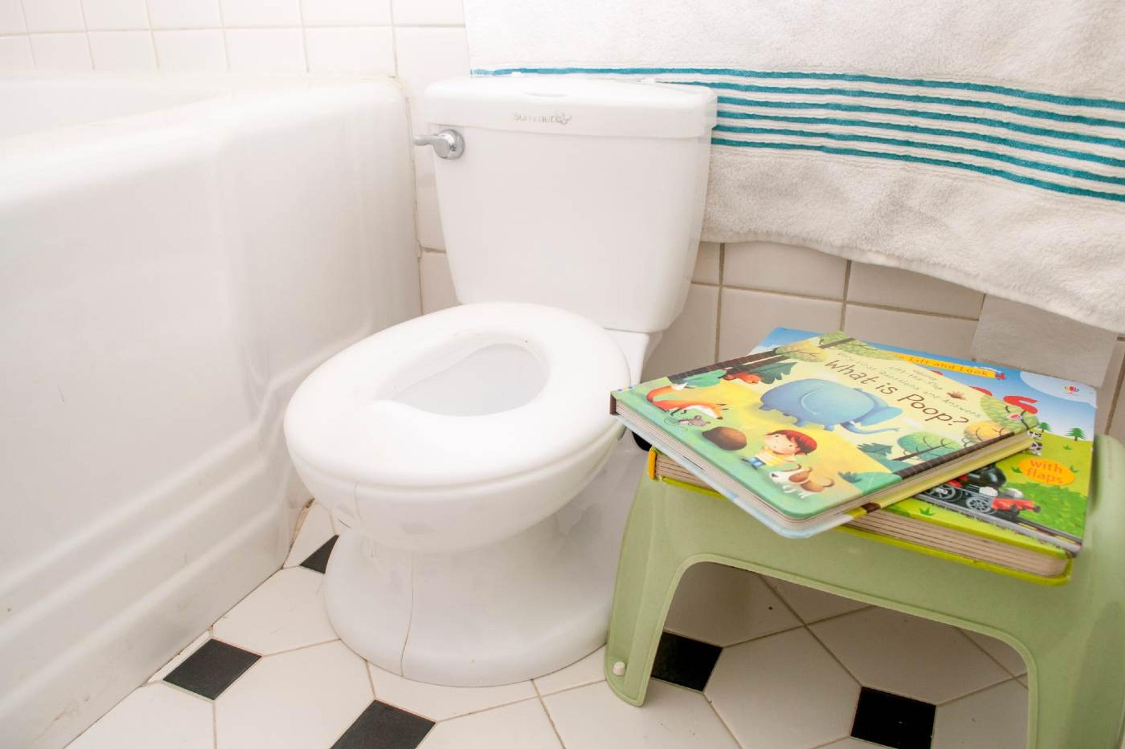 Kids' potty training books stacked on top of a stool next to a toddler-sized toilet.