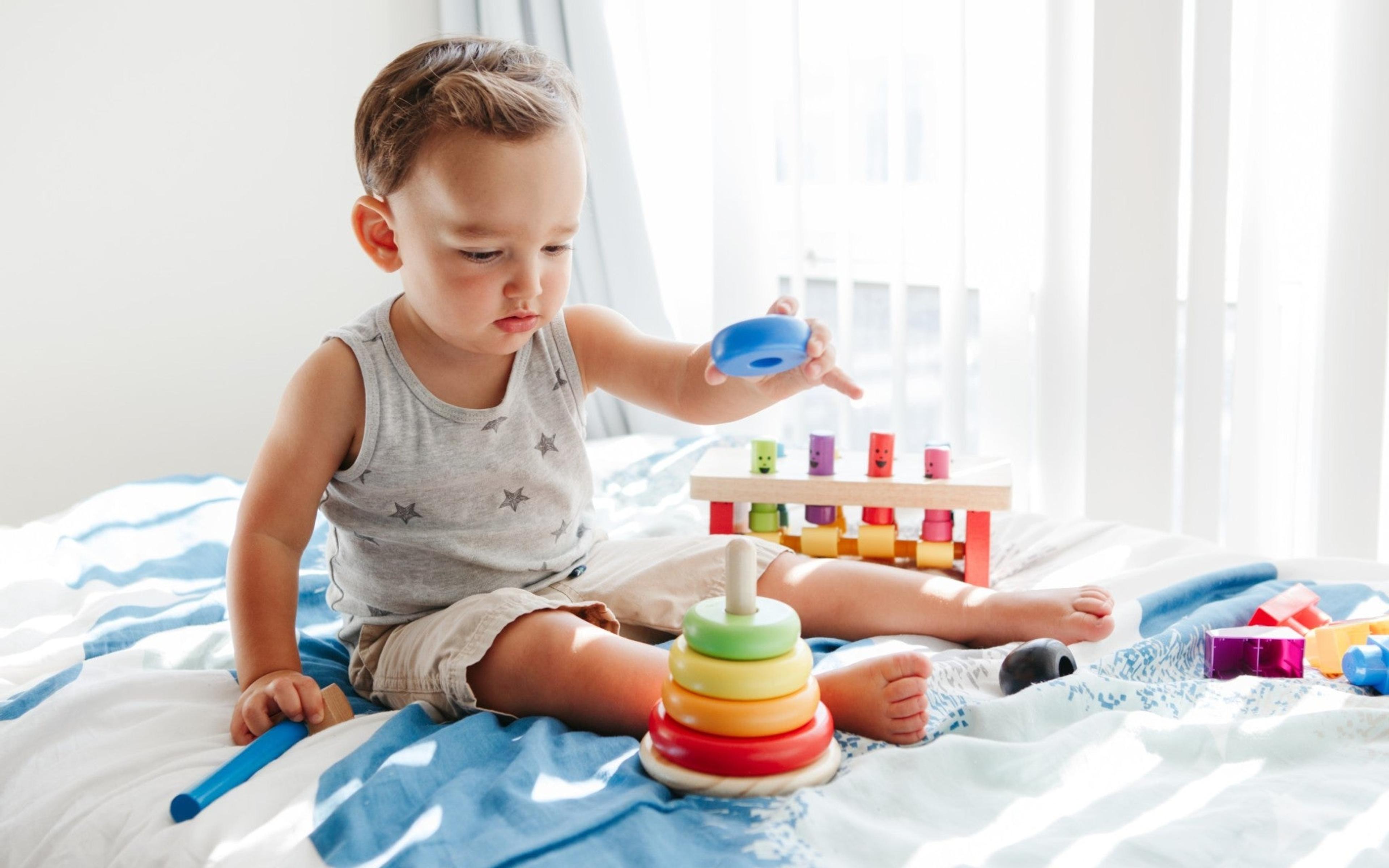 Toddler playing with stacking rings on a bed