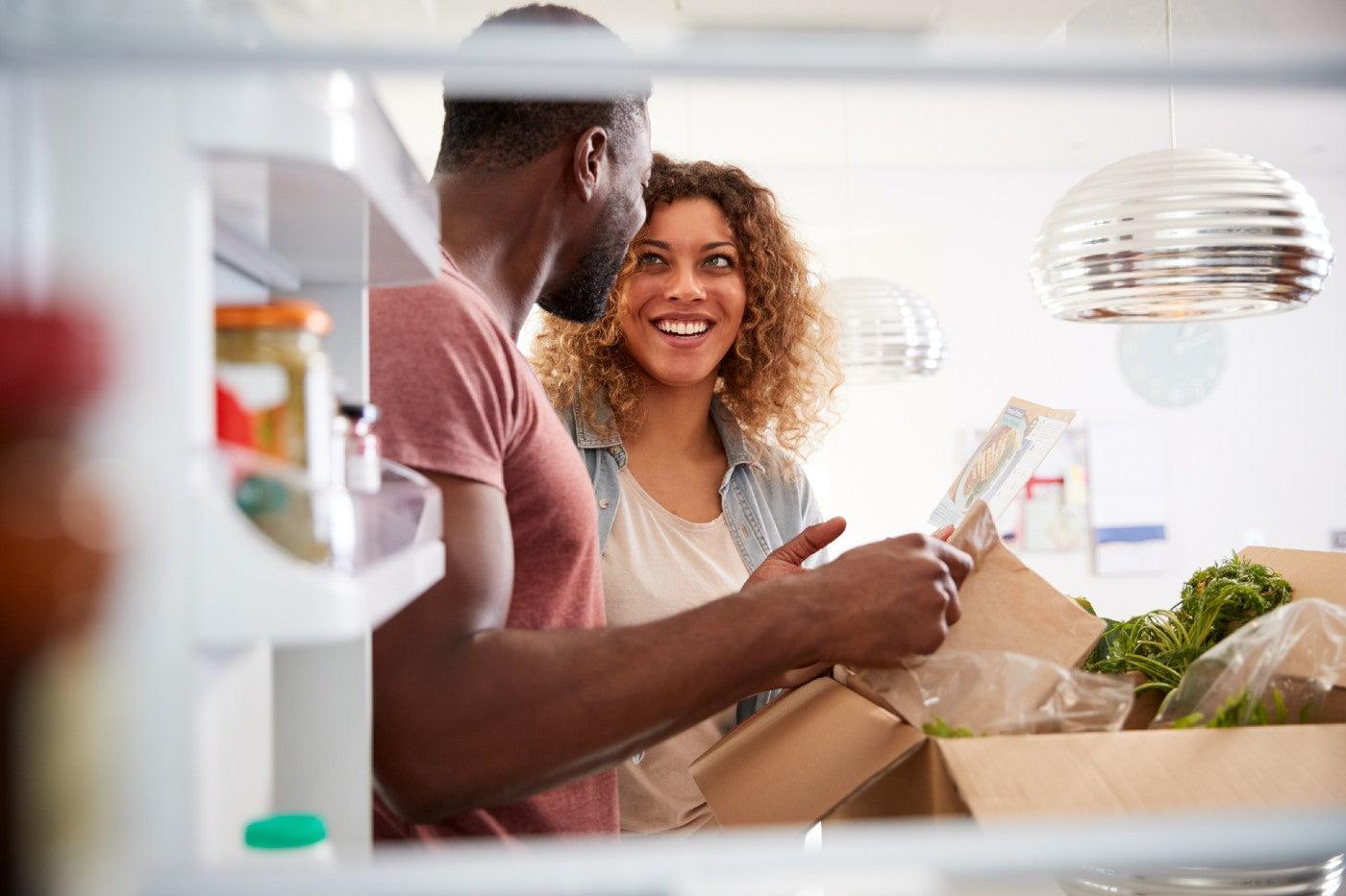 A couple unpacks groceries and puts them in the fridge as part of meal planning