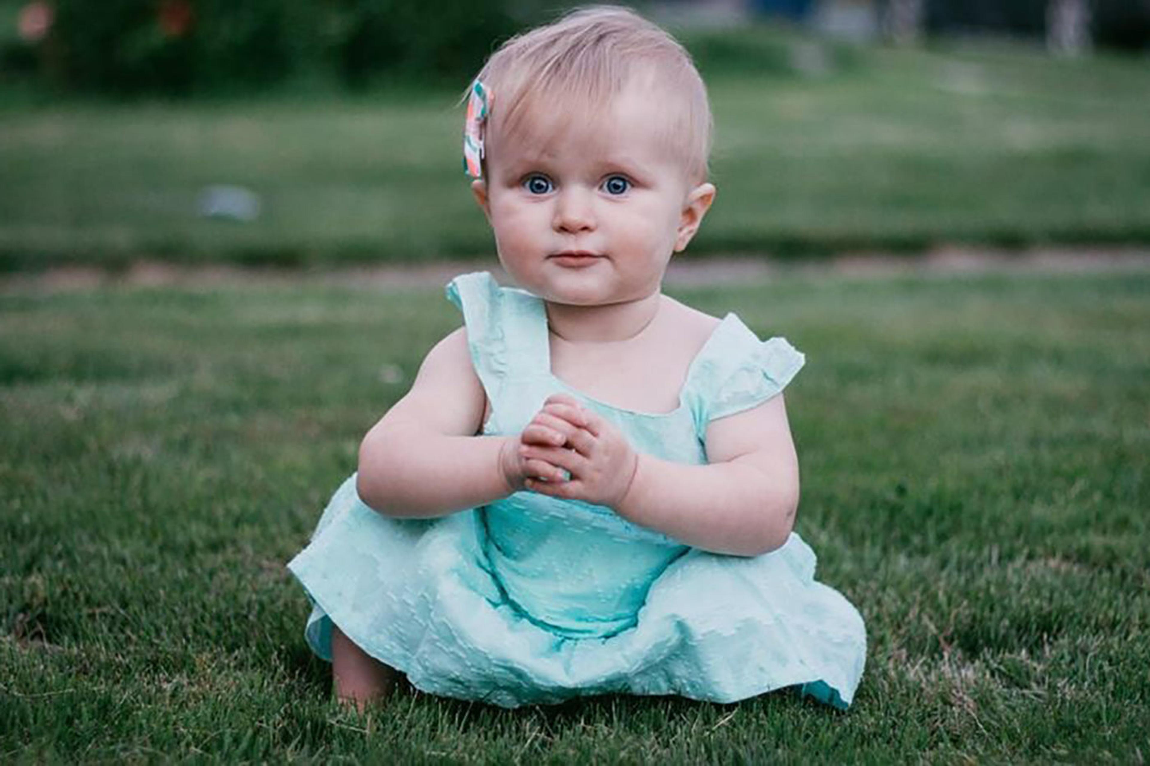 An Irish baby wearing a green dress poses on a lawn