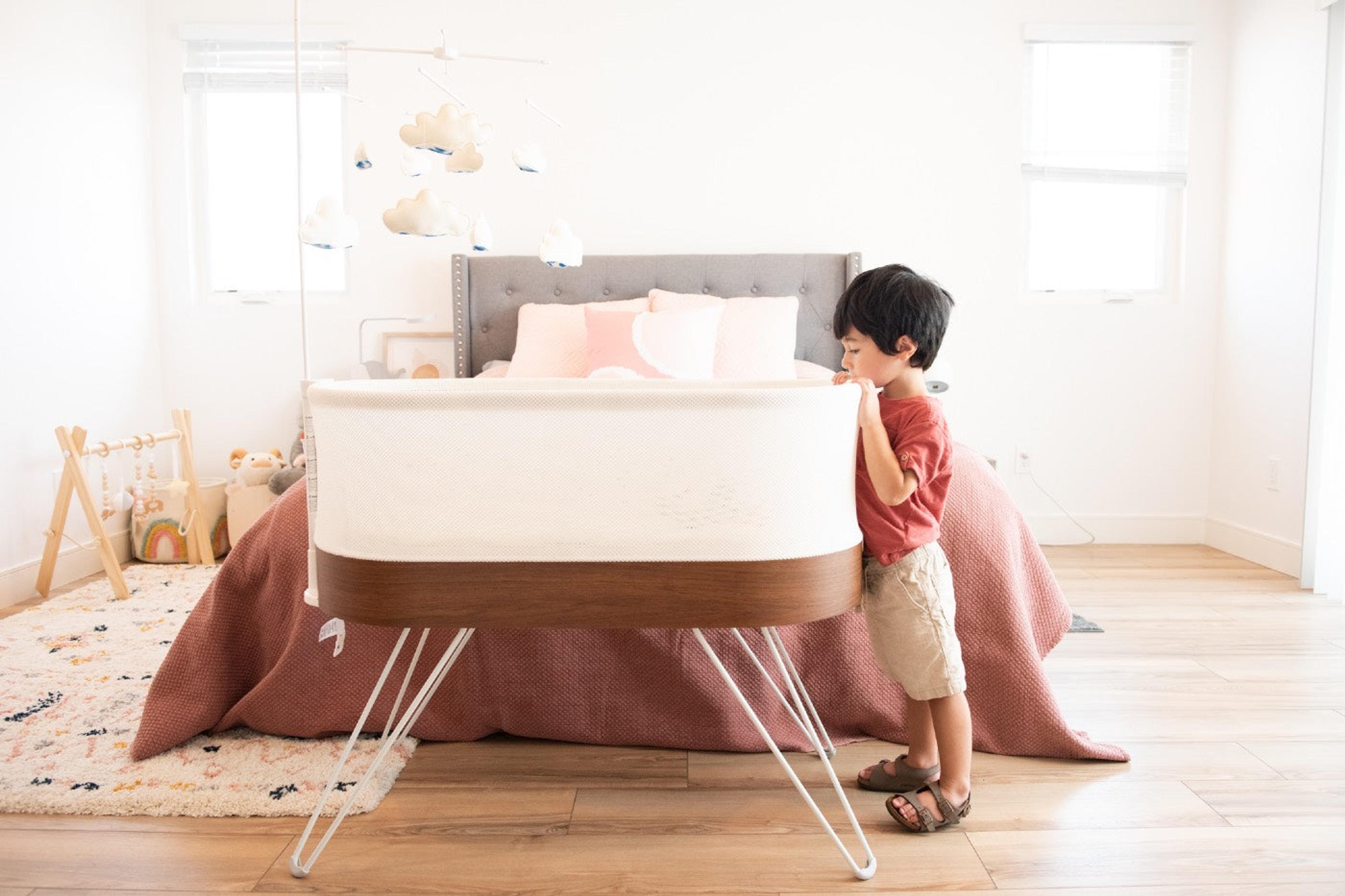 Toddler peers into a SNOO bassinet