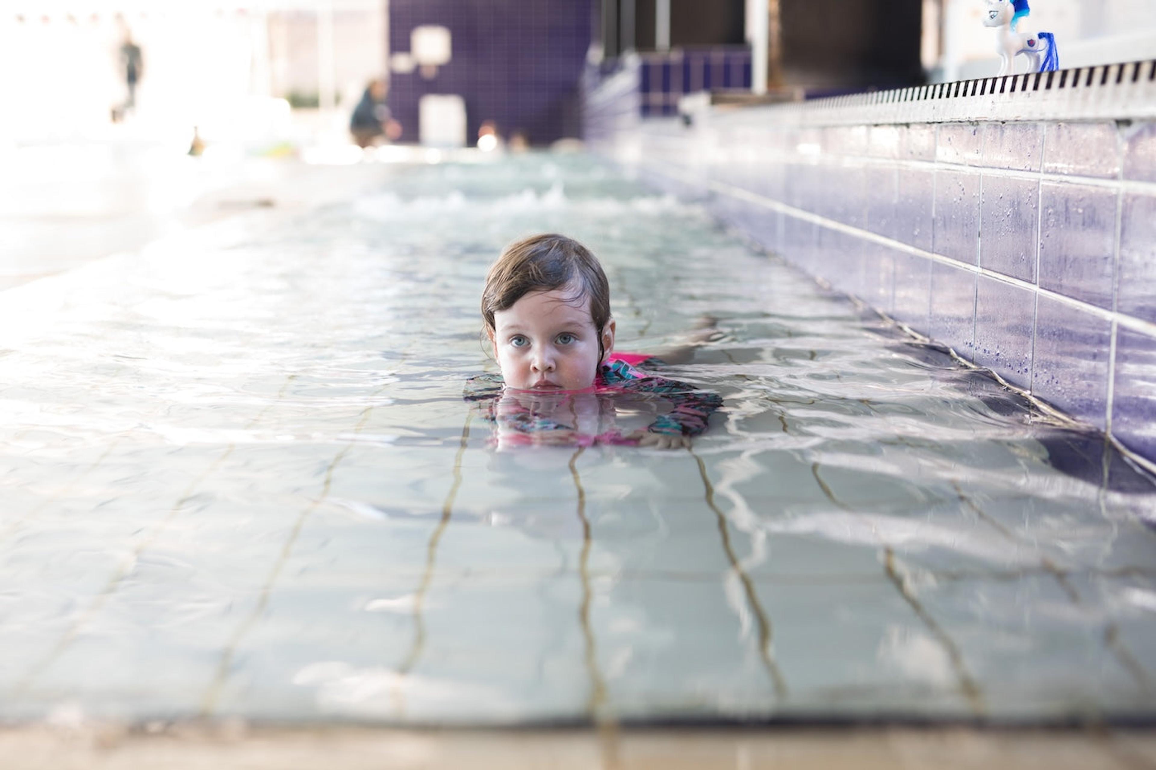 A toddler girl plays in the shallow end of the pool