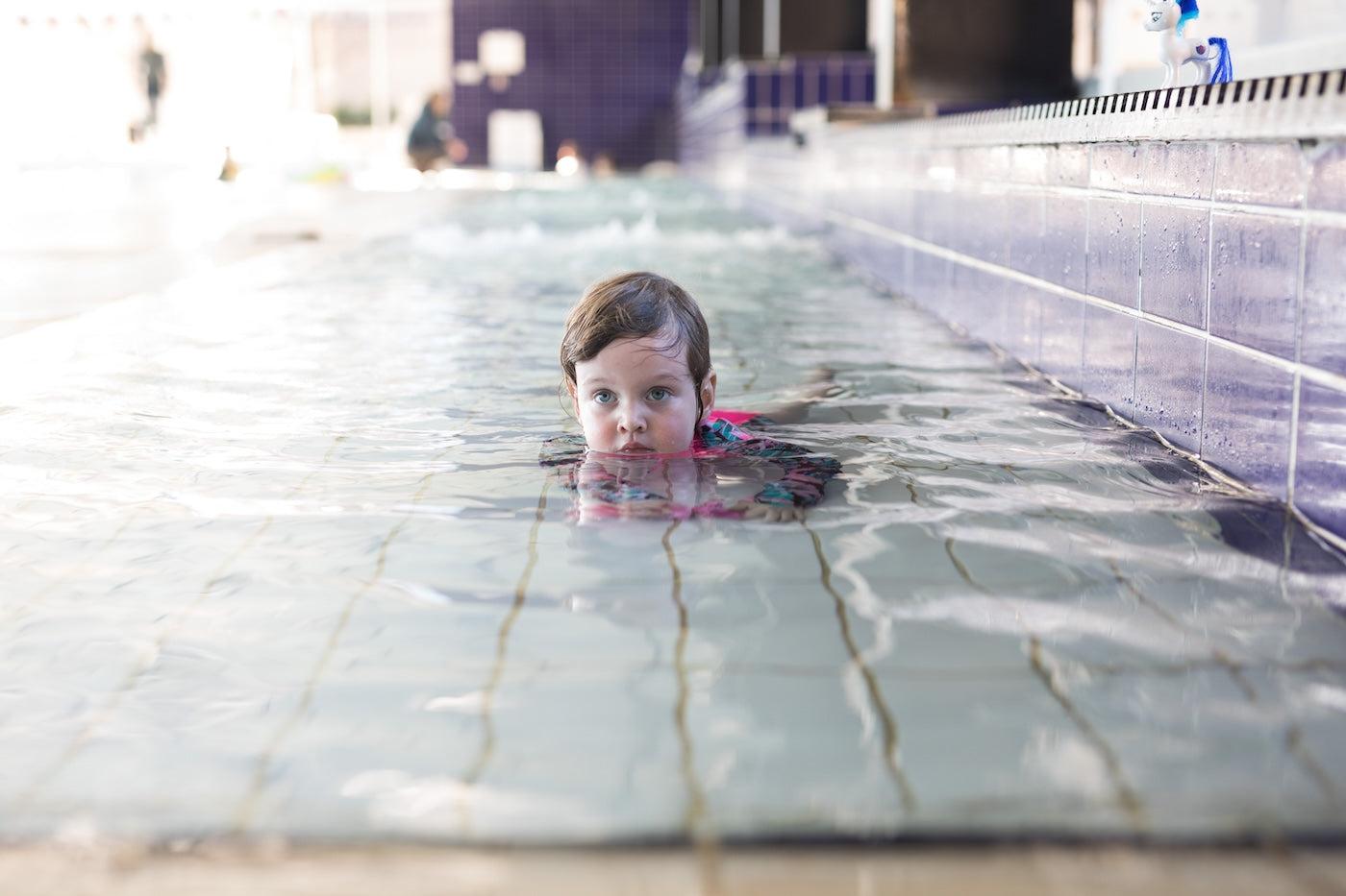 A toddler girl plays in the shallow end of the pool