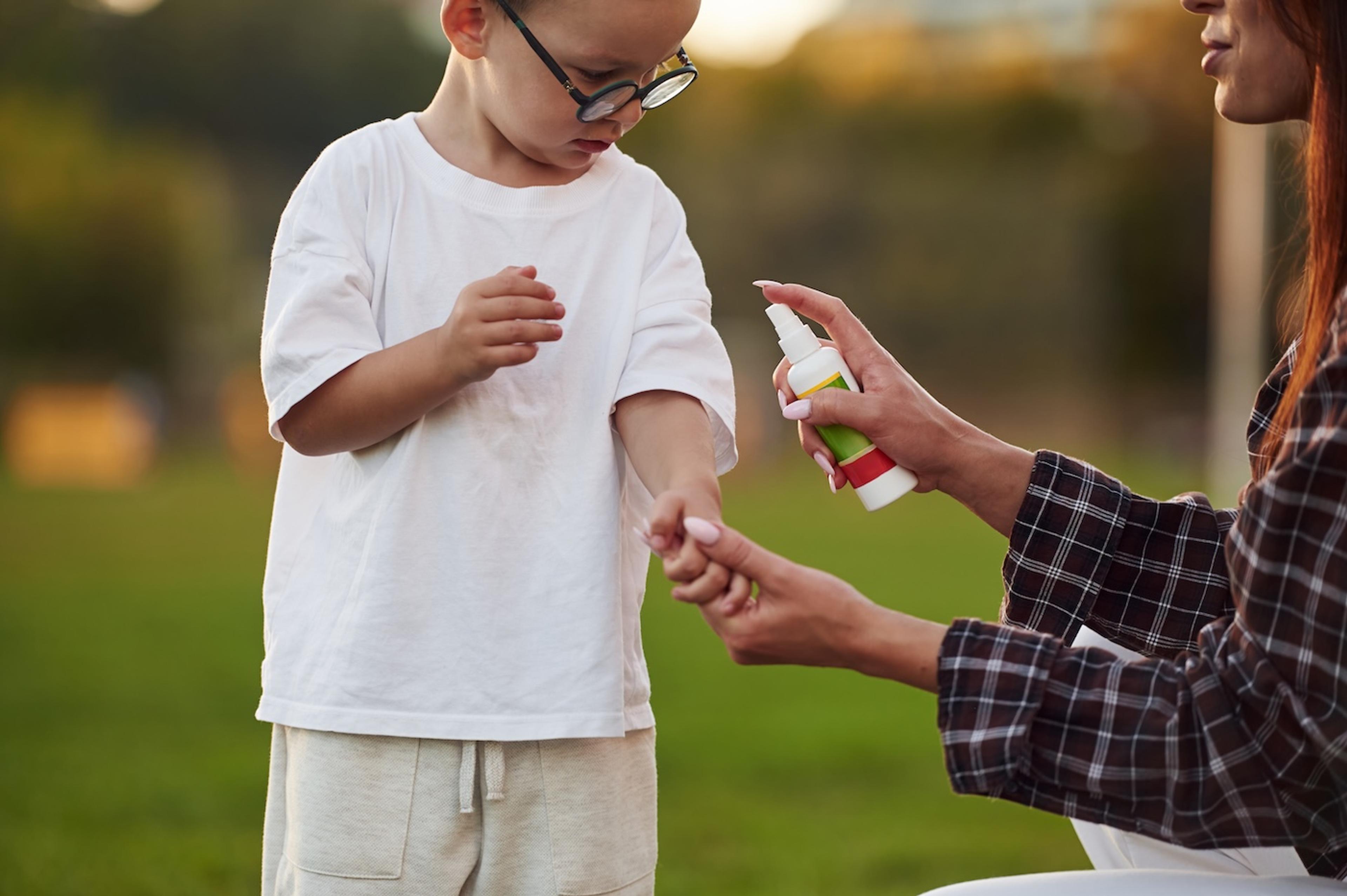 A mom sprays her young son's shirt with insect repellant to keep bugs away