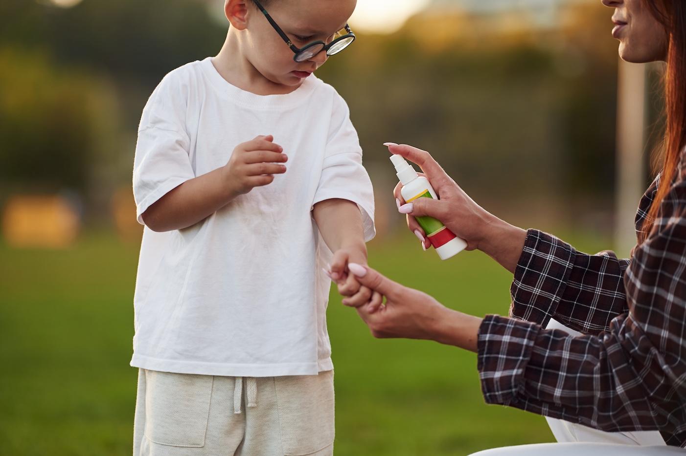 A mom sprays her young son's shirt with insect repellant to keep bugs away